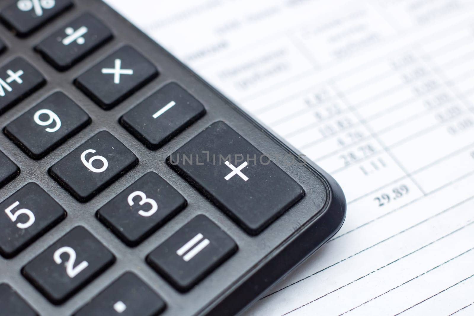 A closeup of a calculator, a peripheral input device, on top of a sheet of paper, office equipment often used with a computer keyboard or personal computer for calculations