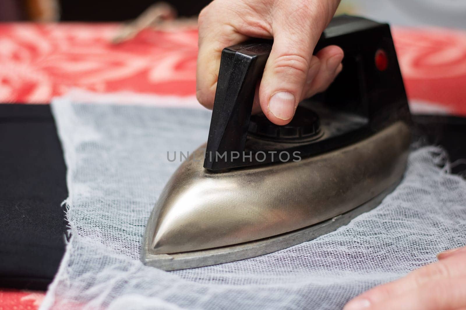 Using their thumb and fingers, a person irons a piece of fabric on a wooden table. The ironing board is covered with carmine leather, a fashionable choice in composite materials