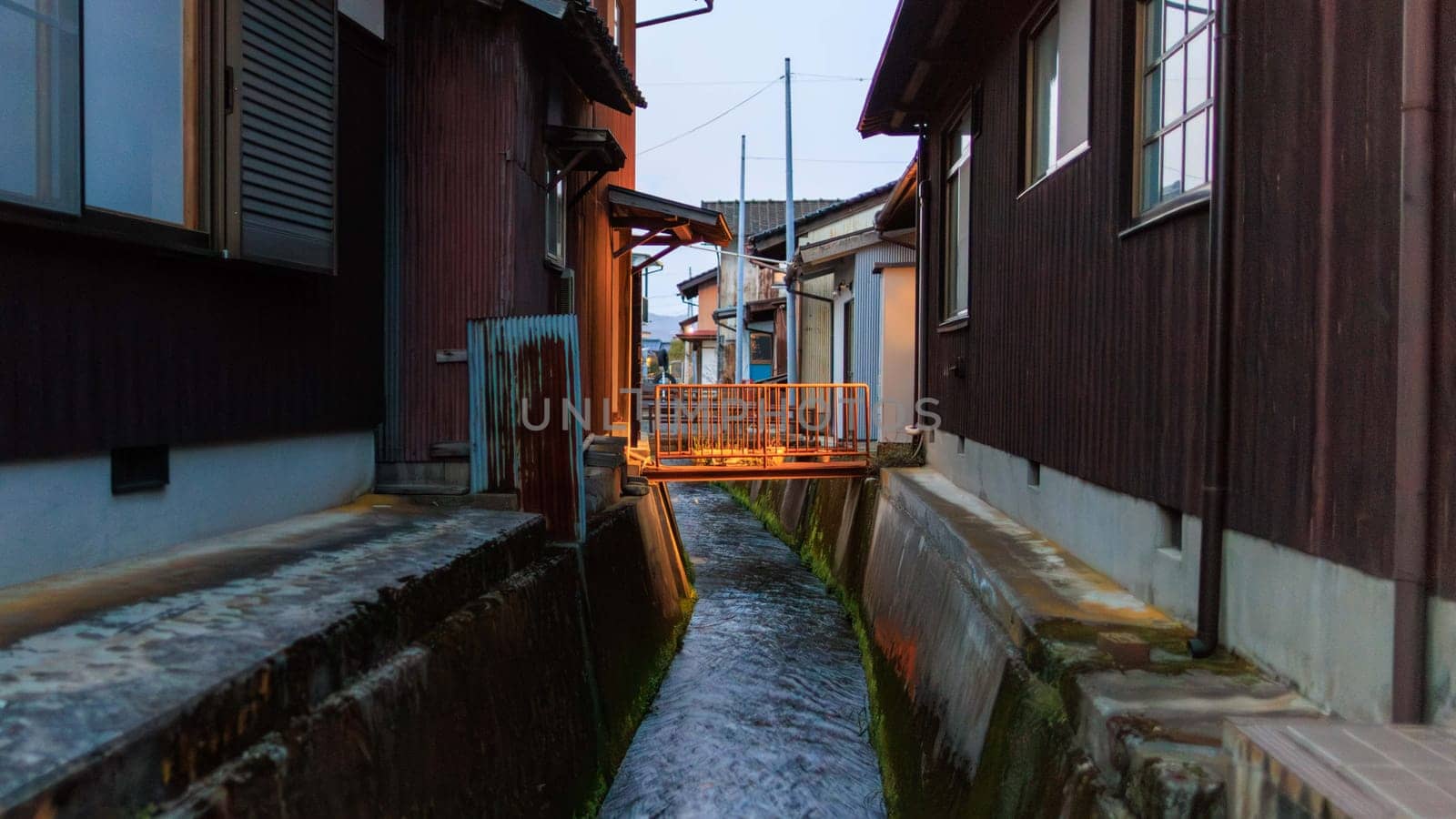 Footbridge over canal between traditional Japanese houses at dusk in Takeda, Japan by Osaze