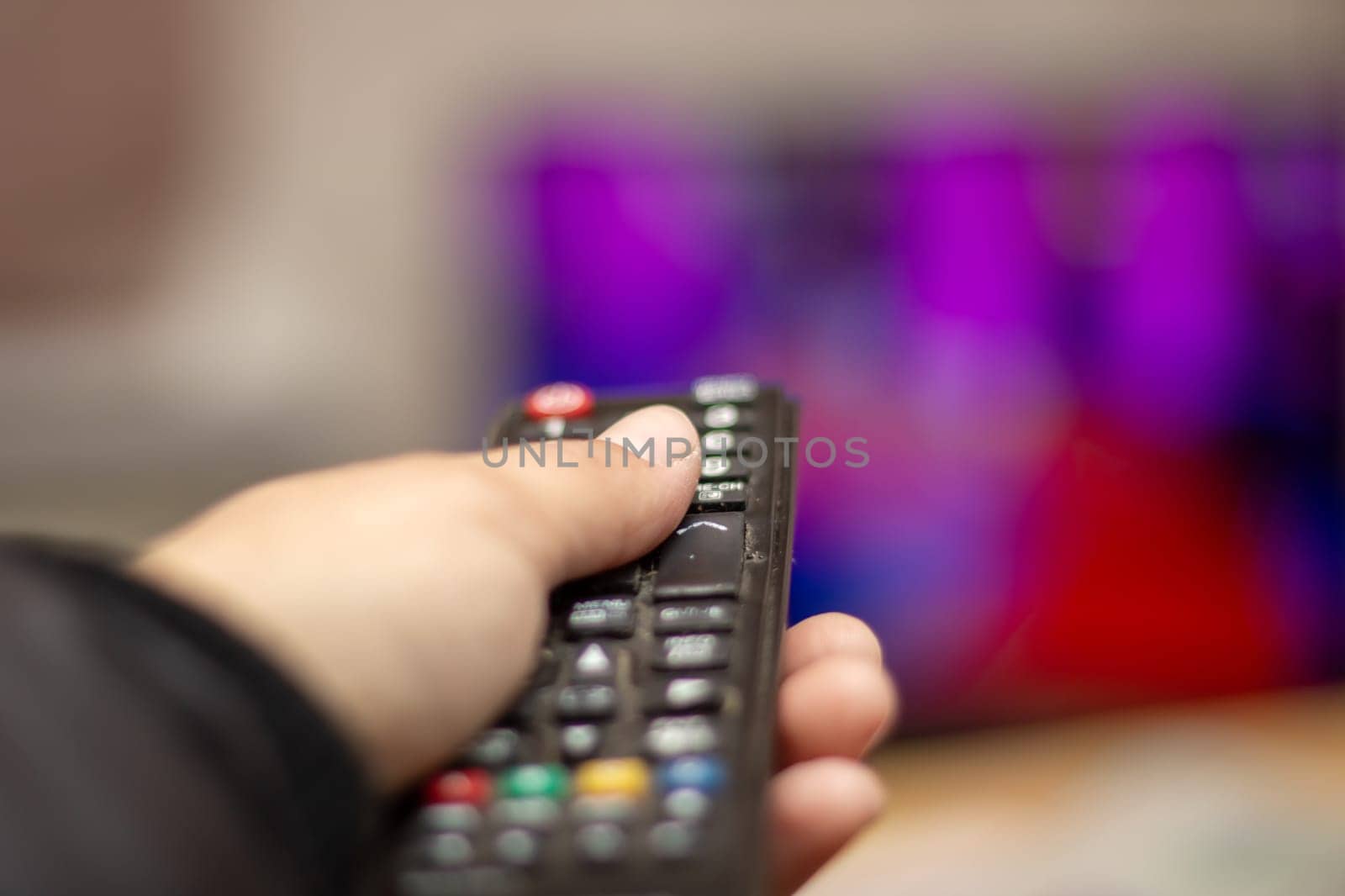 A hand is holding a remote control in front of a television, a gadget used to control electronic equipment like audio and video devices