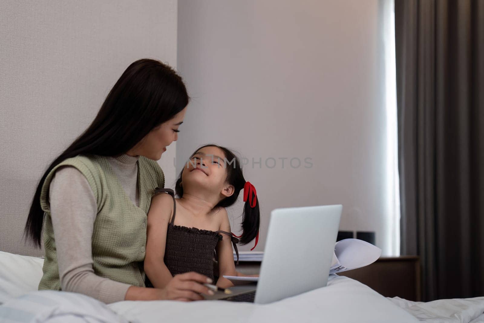Mom work from home with children. Mother working on bed laptop in bedroom with child daughter. Funny authentic lifestyle family moment by nateemee