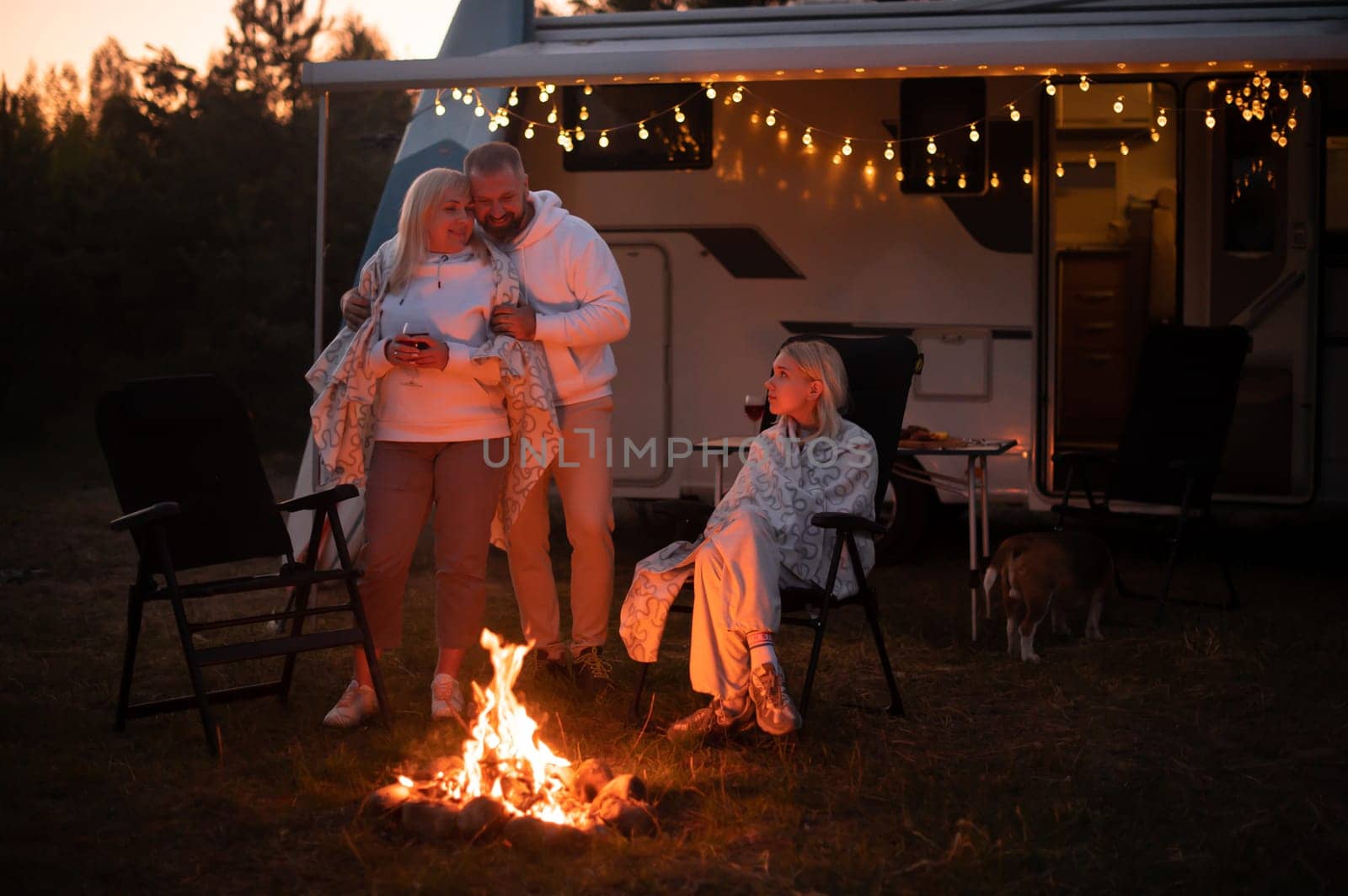 The family is relaxing together by the campfire near their mobile home. Evening family vacation.