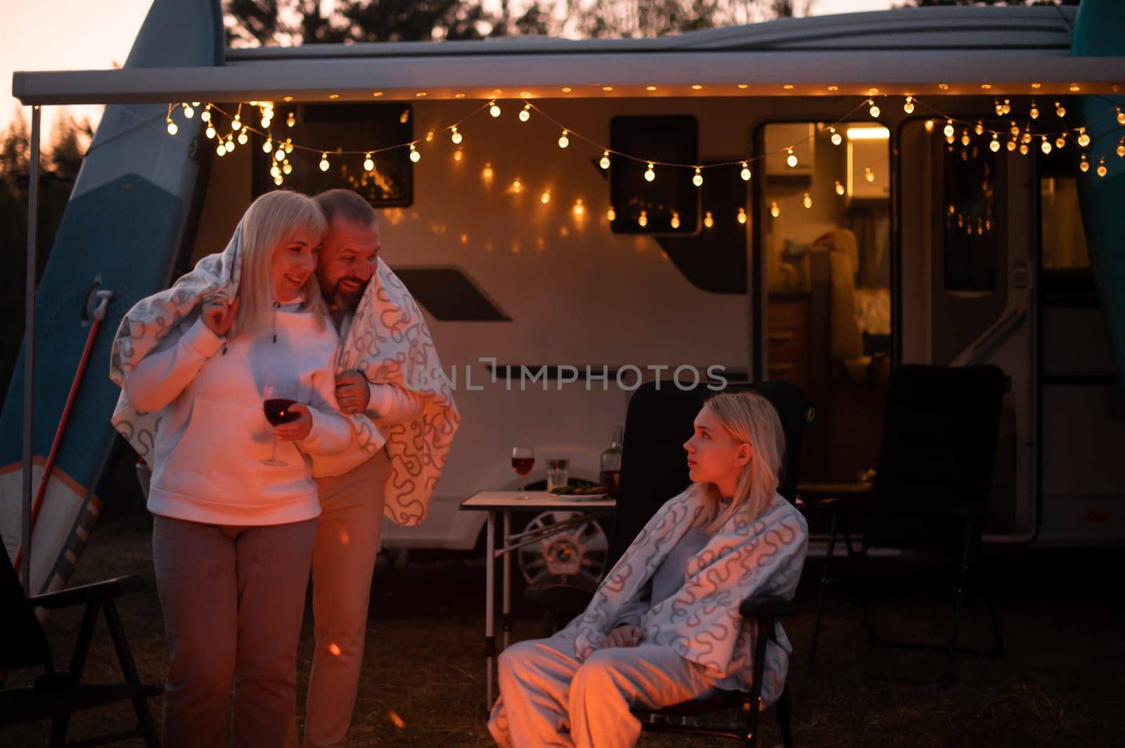 The family is relaxing together by the campfire near their mobile home. Evening family vacation by Lobachad