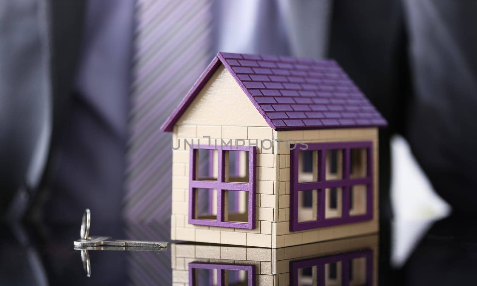 Man in suit and tie and silver key and little toy house at table closeup. New owner, pledge idea for life family solution male arm credit negotiation clerk in office future plan concept