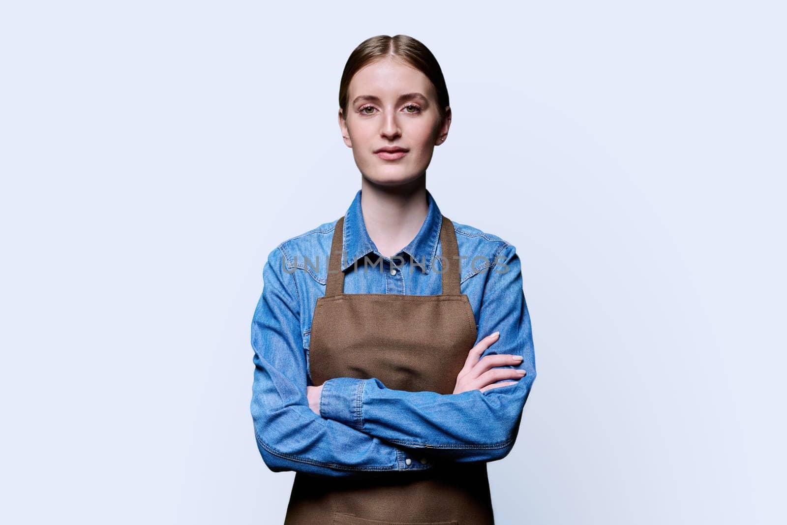 Portrait of young smiling confident woman in apron on white studio background. Successful positive female with crossed arms. Worker, startup, small business, service sector, staff, youth concept