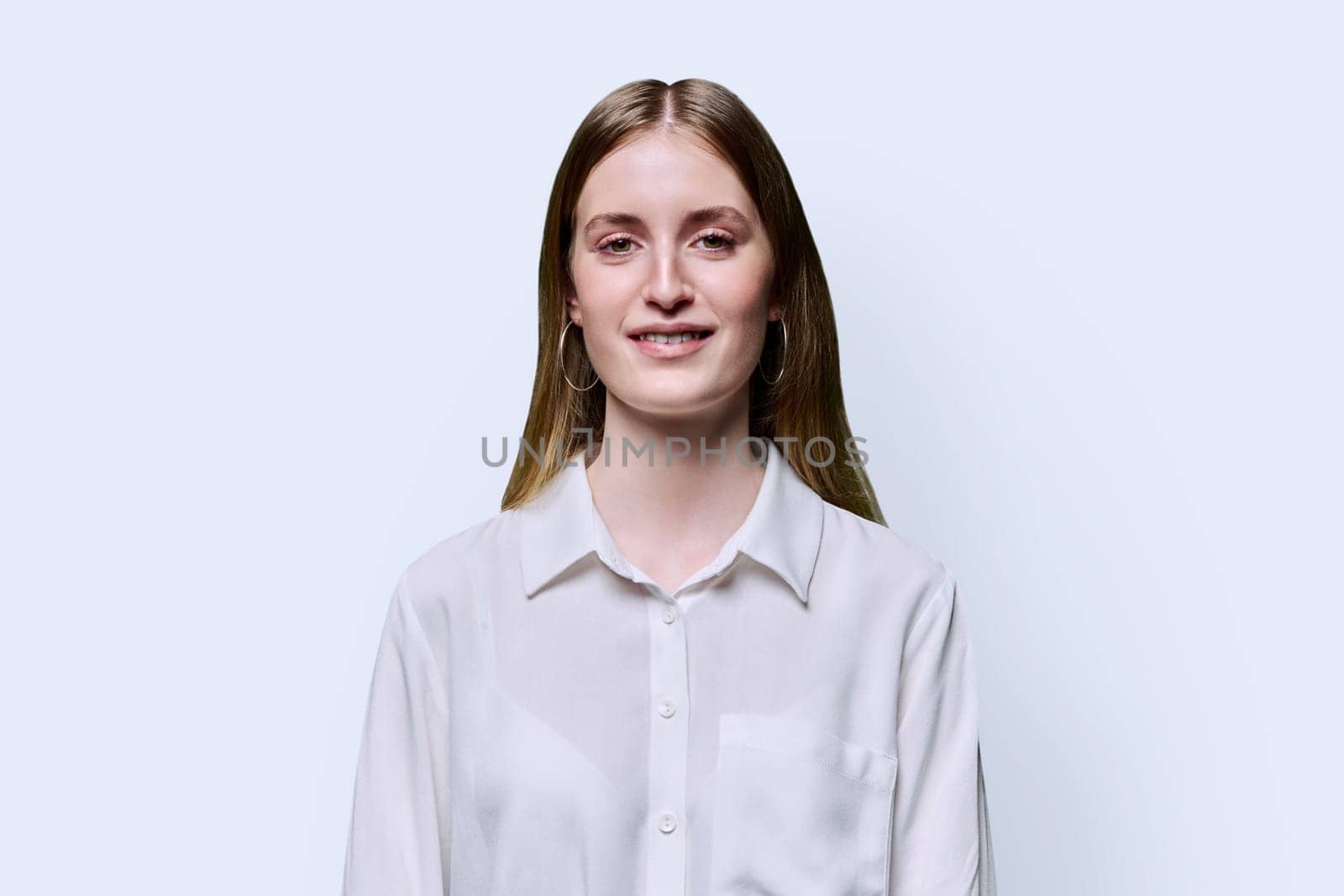 Portrait of young teenage smiling female in white shirt on white studio background. Confident beautiful happy college student girl looking at camera