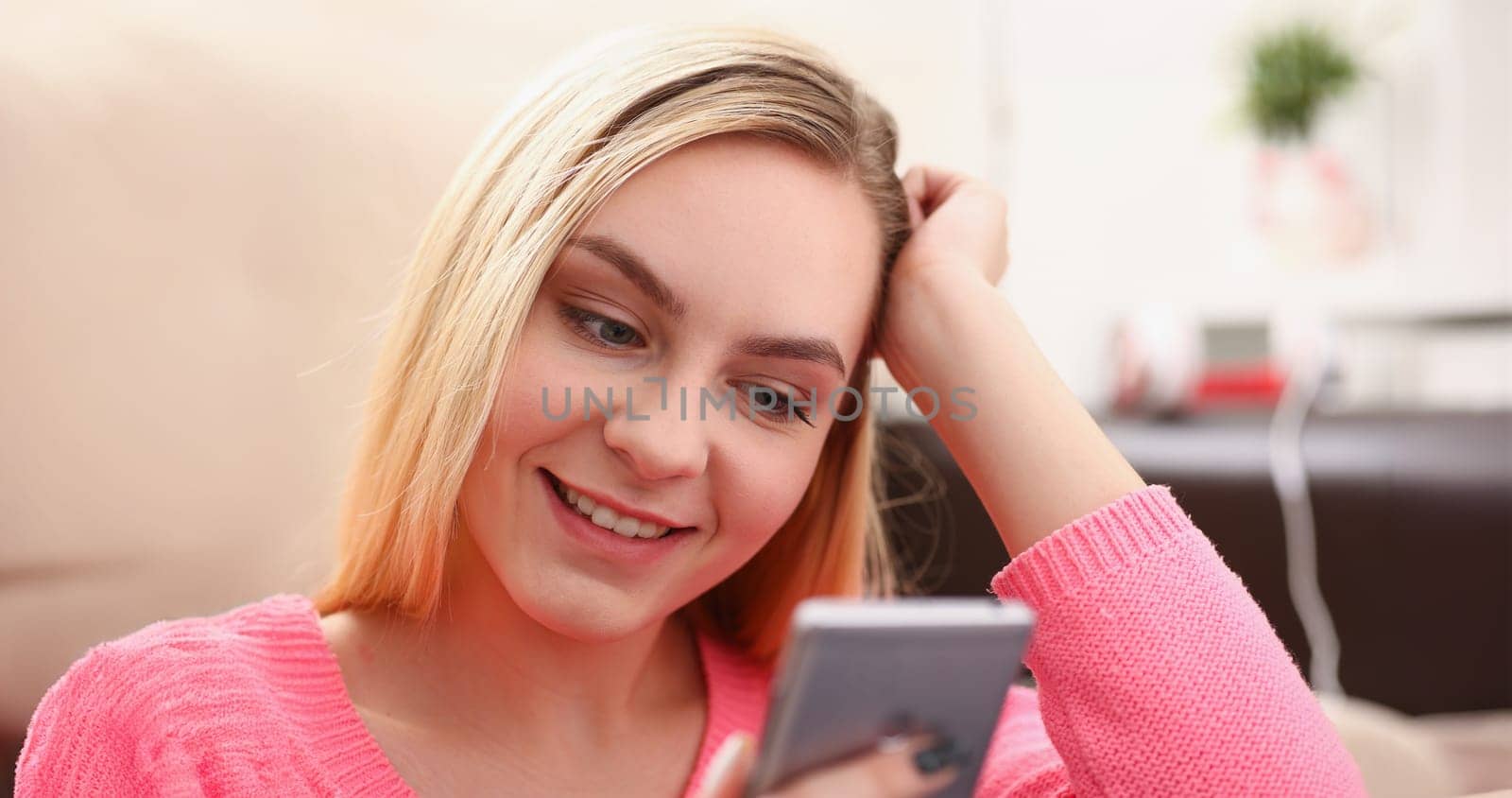 young pretty blond womansit on sofa hold smartphone in hands chat with friends