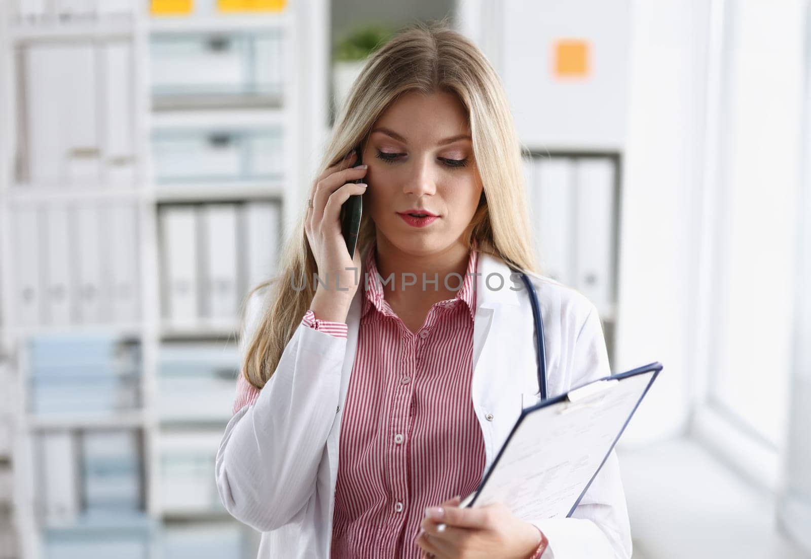 Beautiful female blond doctor talking on phone at the office woman discussing the disease and giving online consultation remote training education