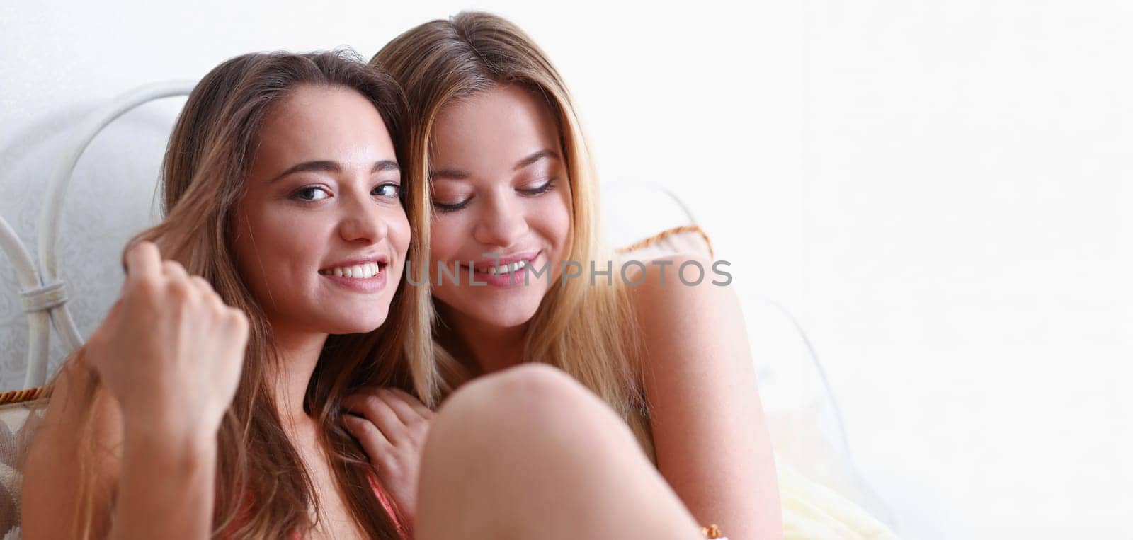 Two happy smiling girlfriends eat popcorn in bed watching TV show early morning holding remote control in hand portrait. Joy cozy tenderness lifestyle football match happiness or tv series concept