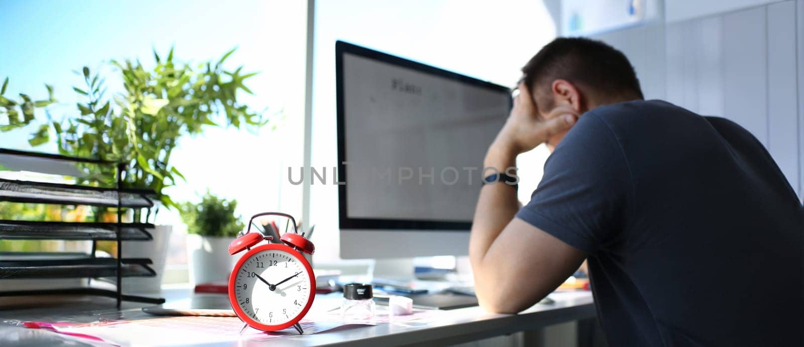 Red alarm clock stand at worktable with thoughtful man in background closeup