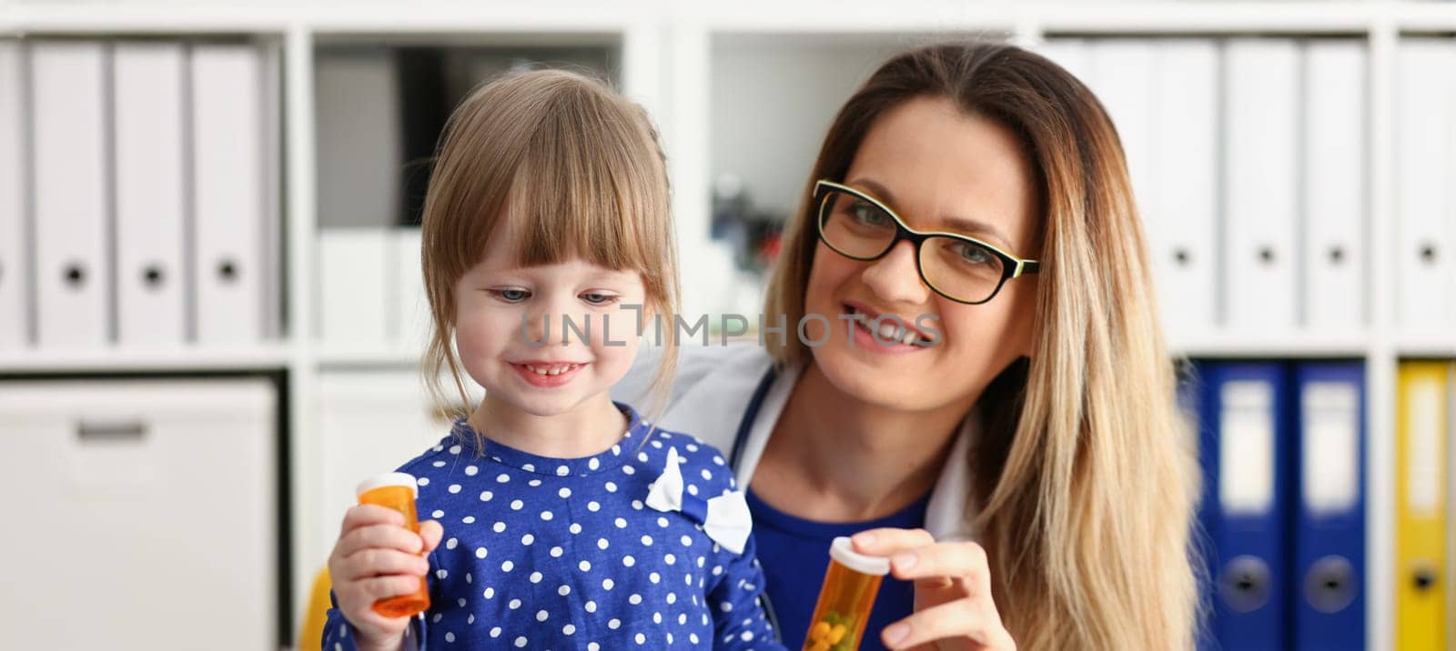 Beautiful smiling female doctor hold in arms pill bottle and offer it to child visitor closeup. Panacea or life save baby from legal store prescribe vitamin medic aid for healthy lifestyle