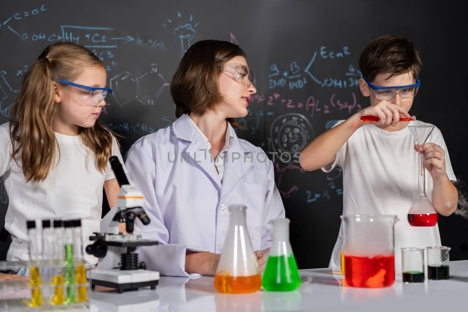 Teacher in support and watch student in laboratory they wear safety glasses, stand and experiment about science of chemistry in STEM class. Student funny do experiment with liquid in tube. Erudition.