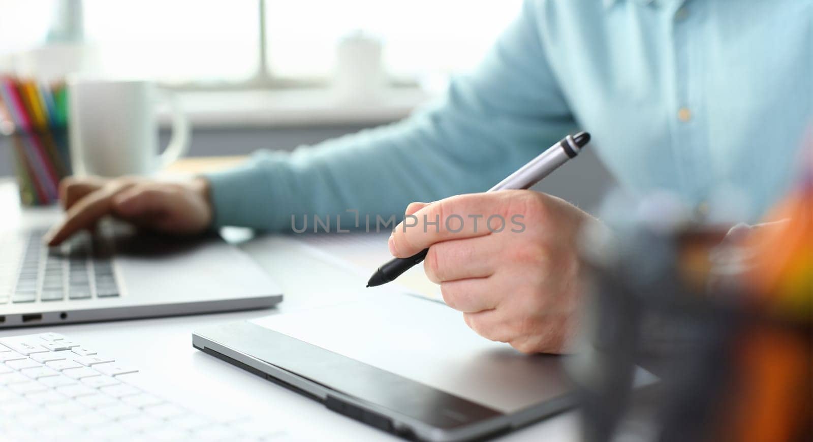 A young designer holds a pen from a tablet in his by kuprevich