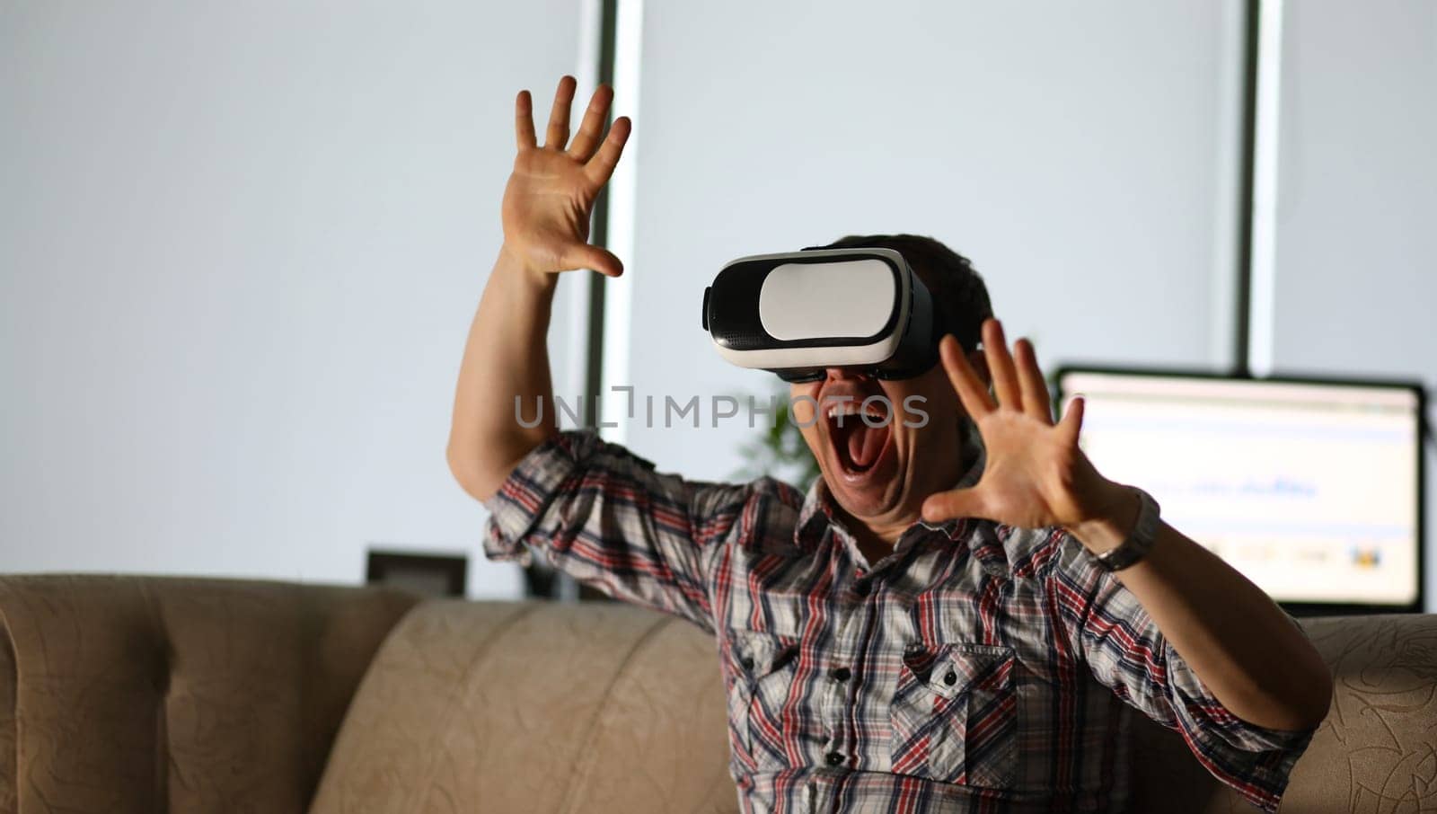 Man sits at home on the couch uses virtual reality glasses rides on a roller coaster screaming in fear. Software tester concept