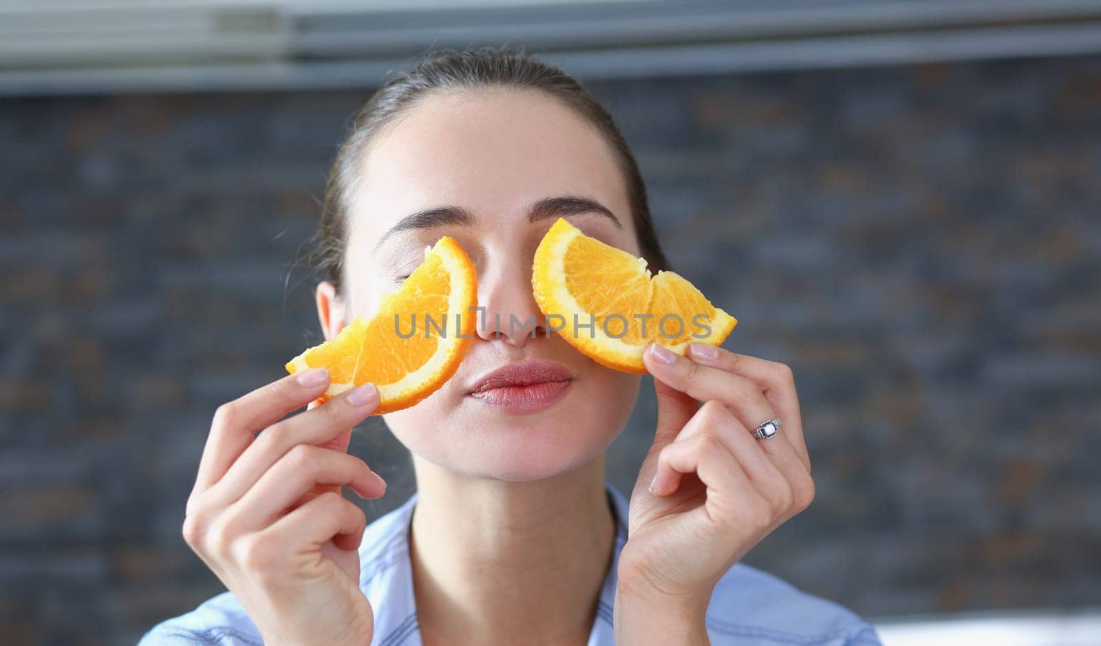 Beautiful brunette smiling woman eat sliced raw tasty orange half at kitchen in the morning portrait. Weight loss beauty fit concept