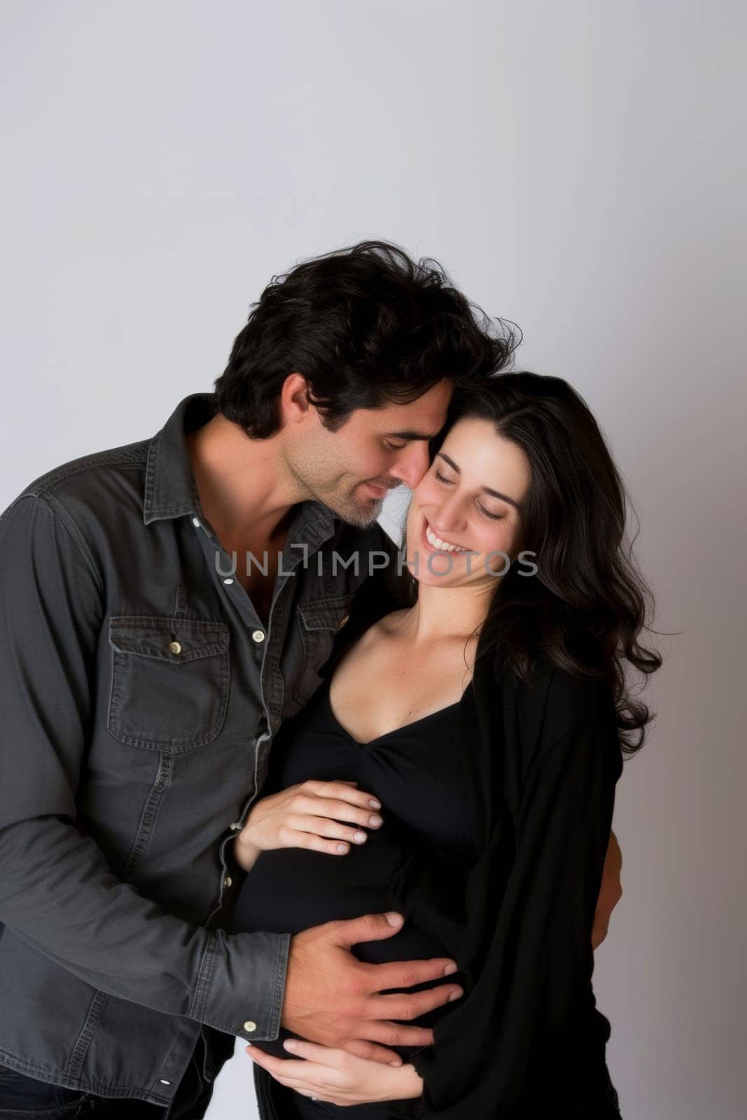 Expectant couple sharing a loving moment, with hands on the pregnant belly, standing against a neutral background