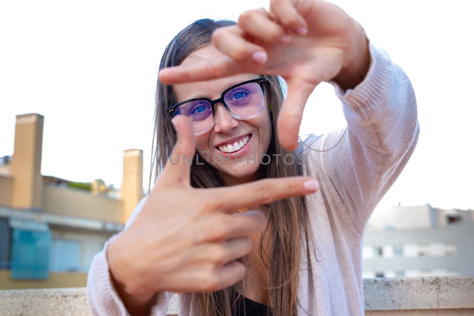 Smiling woman looking through finger frame during sunny day outdoors by mariaphoto3