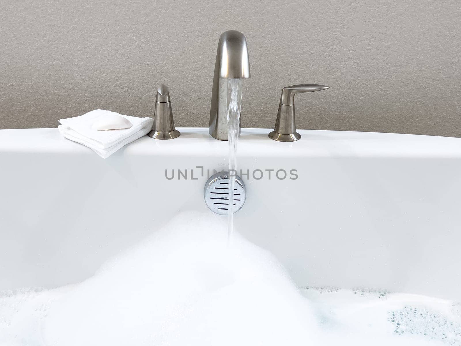 Modern White Bathtub Filled with Running Water from a Brushed Nickel Faucet by arinahabich