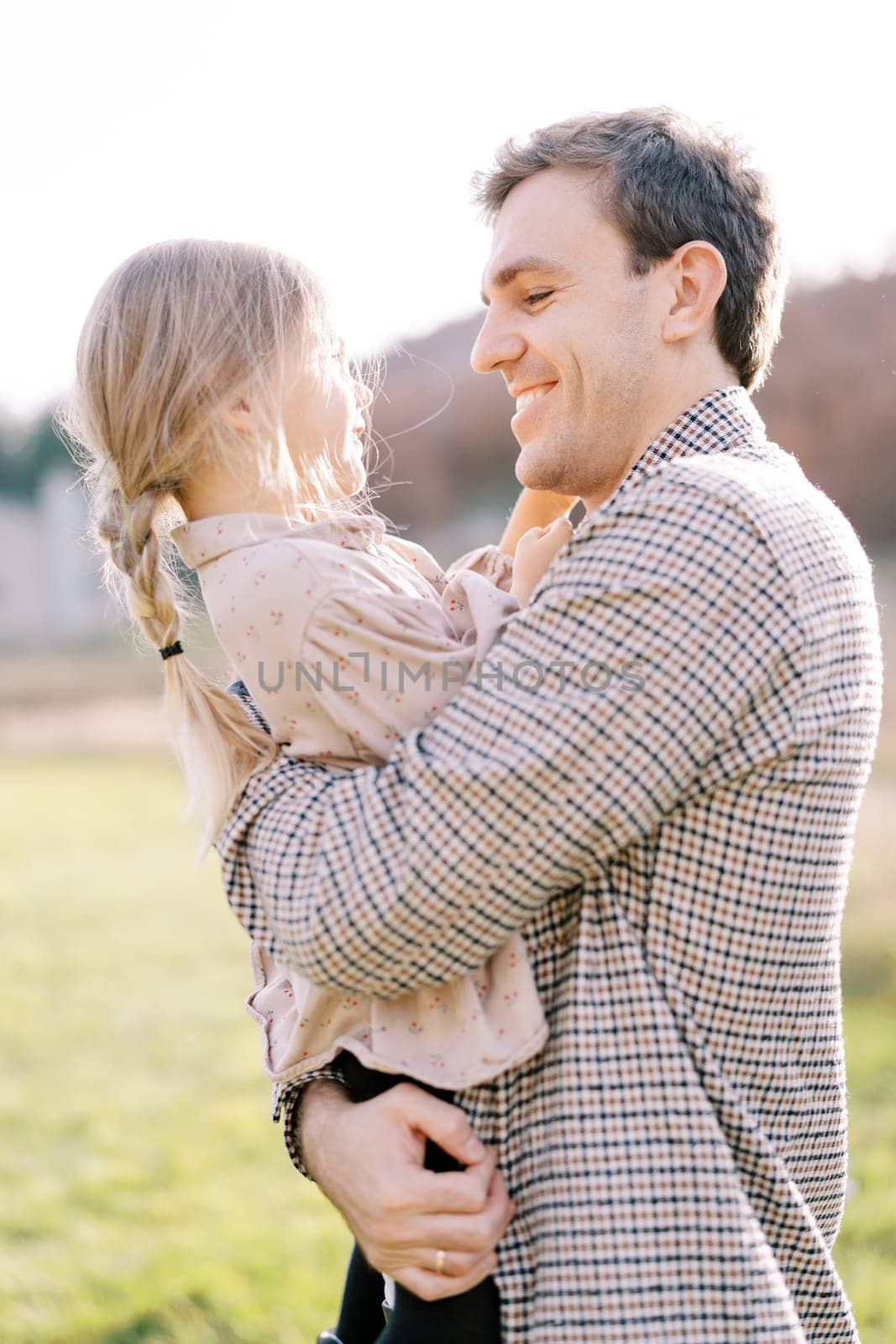 Smiling dad looking at little girl in his arms while standing on the lawn. High quality photo