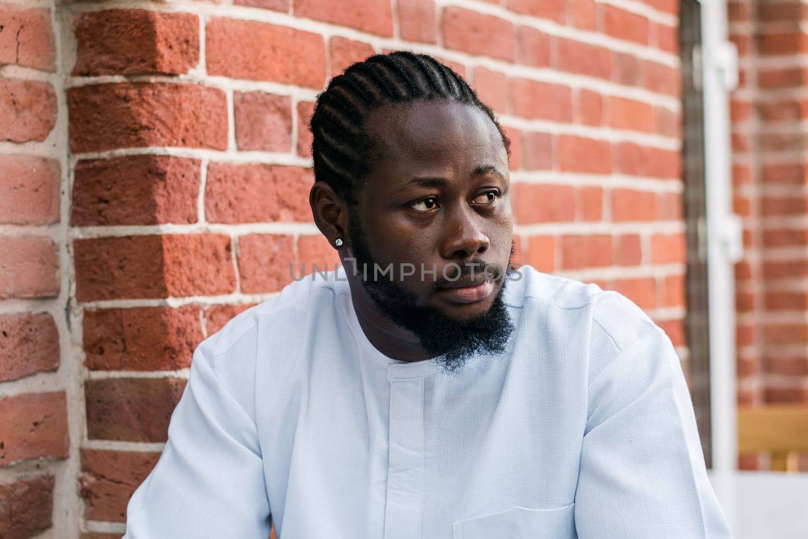 Close up portrait of a happy african american man smiling wearing ethnic dashiki clothes outdoor in summer street colourful brick wall. Millennial generation student and youth. Copy space.