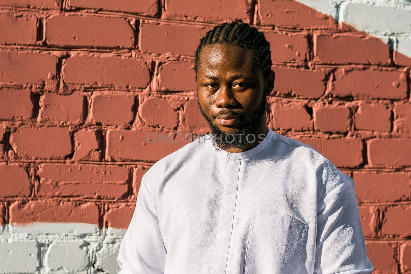 Close up portrait of a happy african american man smiling wearing ethnic dashiki clothes outdoor in summer street colourful brick wall. Millennial generation student and youth. Copy space by Satura86