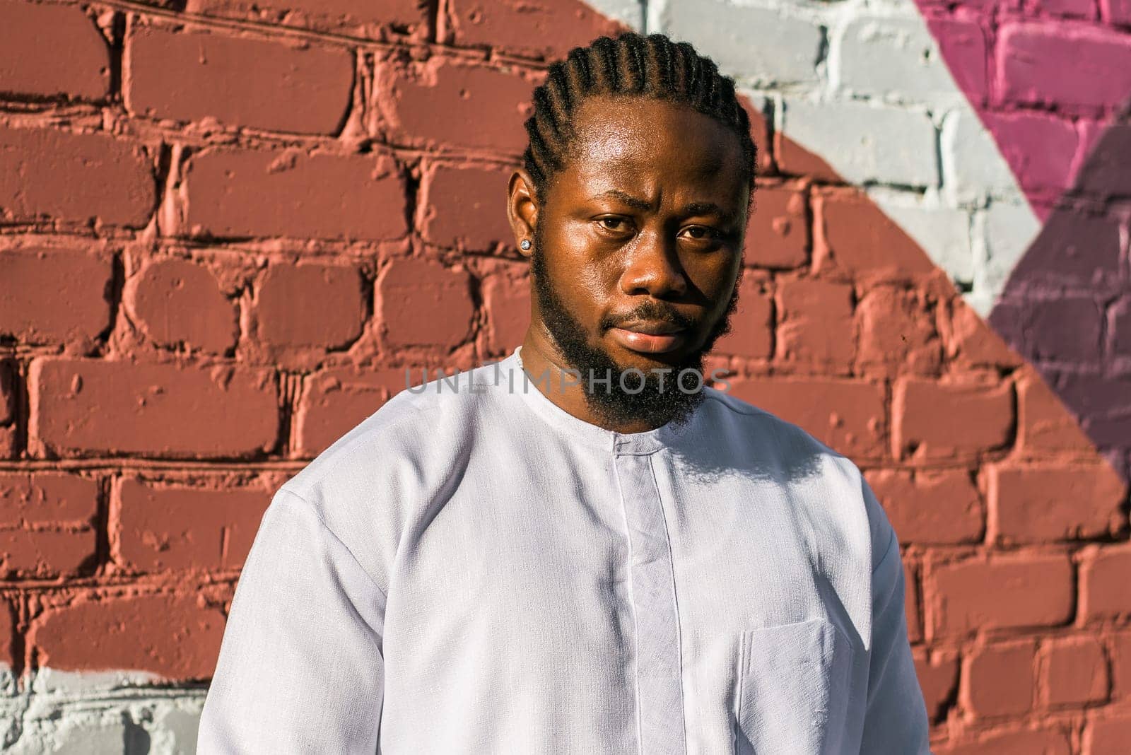 Close up portrait of a happy african american man smiling wearing ethnic dashiki clothes outdoor in summer street colourful brick wall. Millennial generation student and youth. Copy space by Satura86