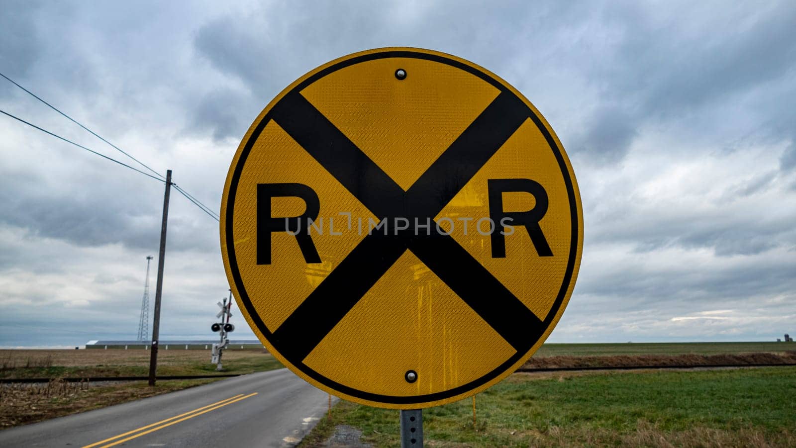 A yellow and black sign with the letters R and X on it. The sign is on a road and is surrounded by a field
