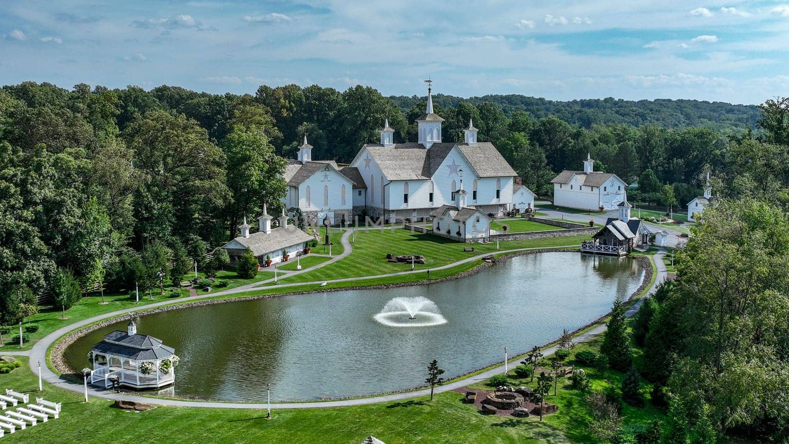 Elizabethtown, Pennsylvania, USA, August 11, 2023 - Aerial View Showcasing A Cluster Of Traditional White Orthodox Churches With Cross-Topped Domes, Arranged Around A Curved Pond With A Fountain, Amidst Green Trees And Neatly Arranged White Benches