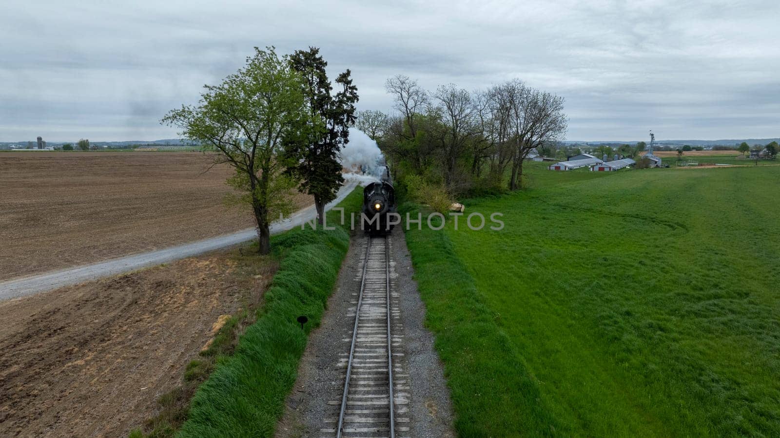 Train is traveling down track next to field. The train is black and steam is coming out of the front by actionphoto50