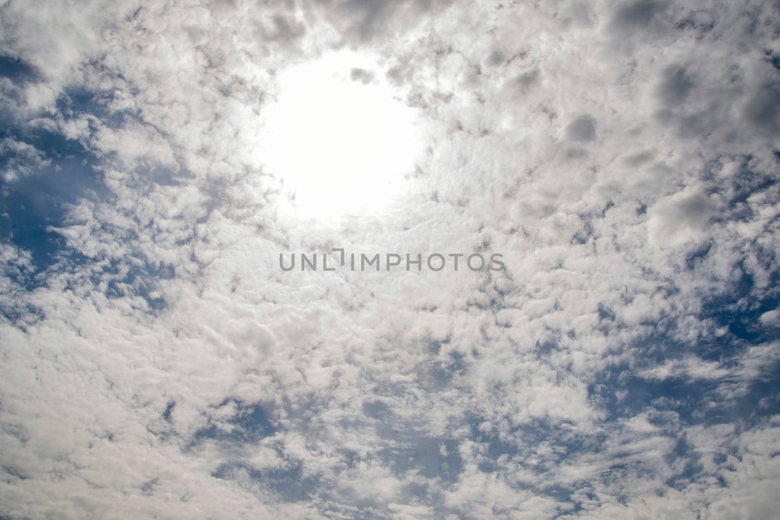 Sky is cloudy and the sun is shining through the clouds. The sun is creating bright spot in the sky by actionphoto50