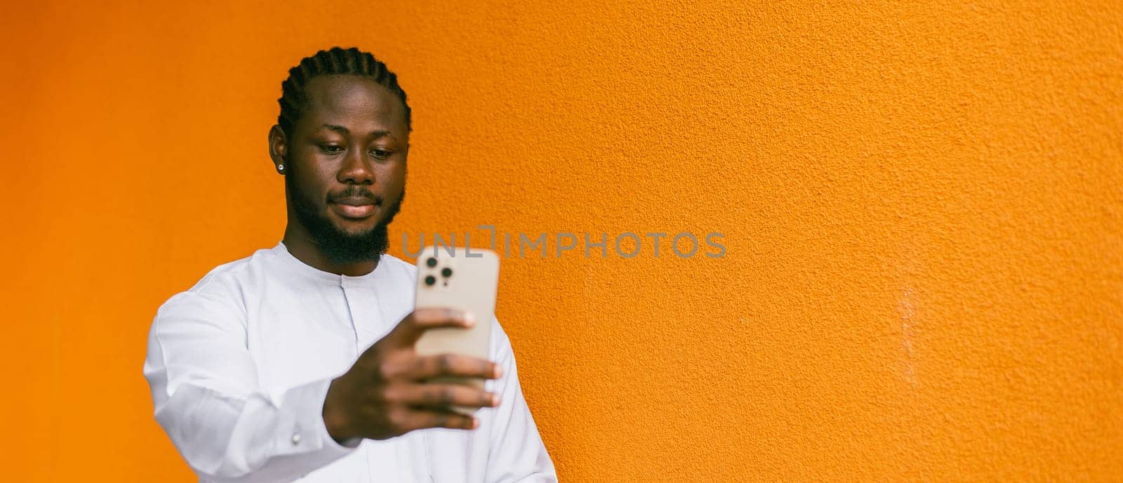 Banner Happy young African American man in dashiki ethnic clothes taking selfie on orange wall background copy space. Millennial generation student and youth