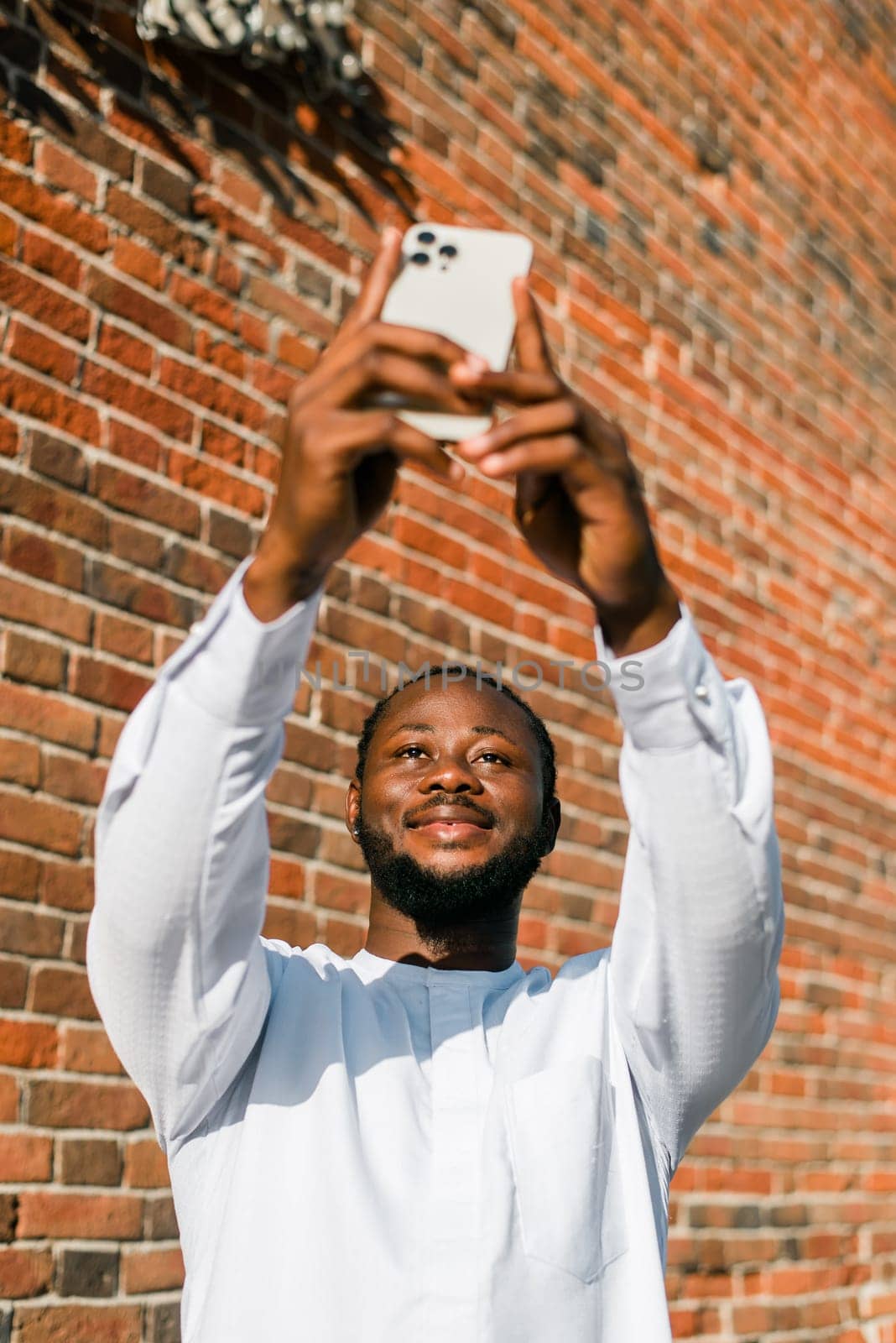 Happy young African American man in dashiki ethnic clothes taking selfie on brick wall background. Millennial generation student and youth