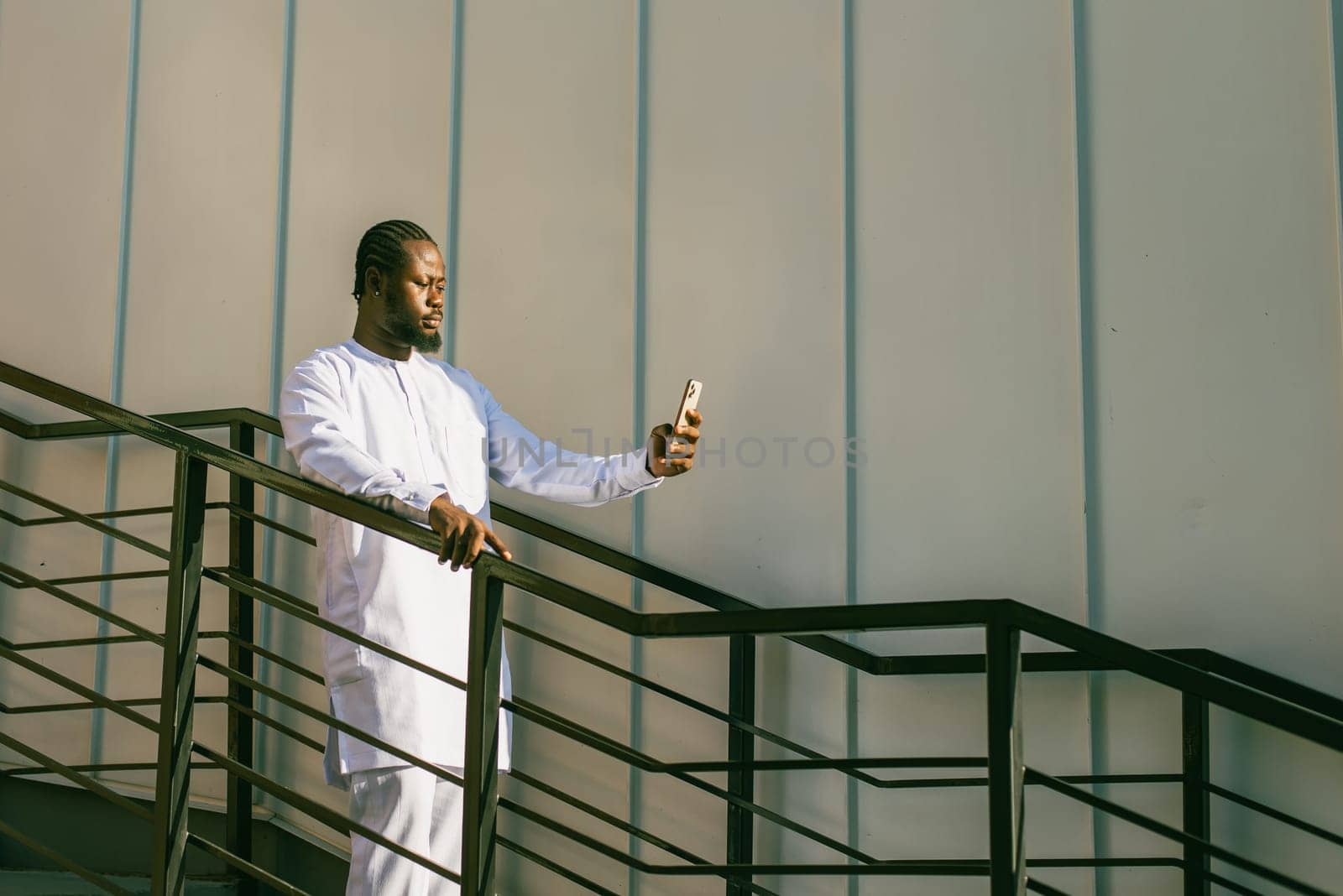 Happy young African American man in dashiki ethnic clothes taking selfie on wall and stairs background copy space. Millennial generation student and youth. by Satura86