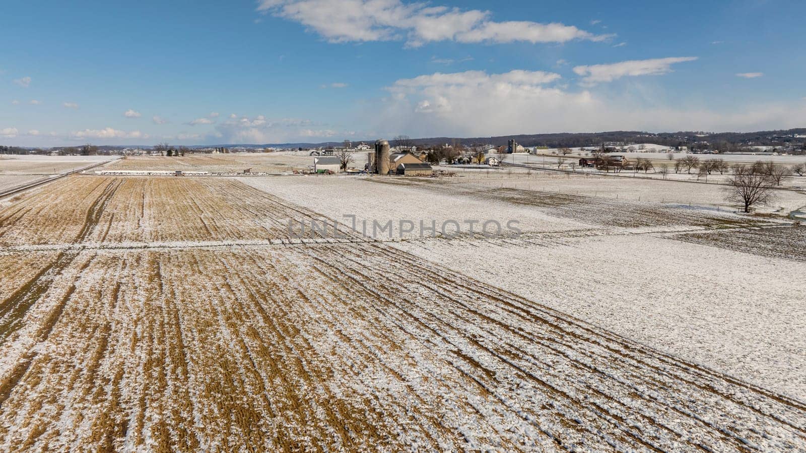 Aerial View Of Snow-Speckled Agricultural Fields And Farm Buildings. by actionphoto50