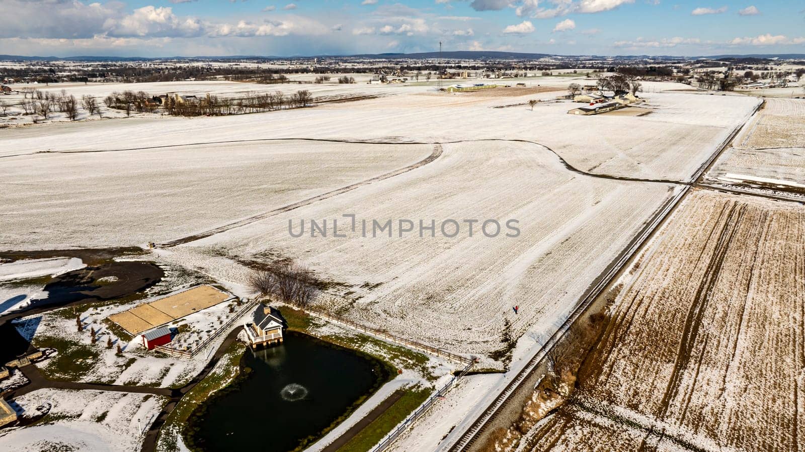 AnAerial View Of A Frosty Landscape Featuring A Pond, Railroad, And Snowy Fields.