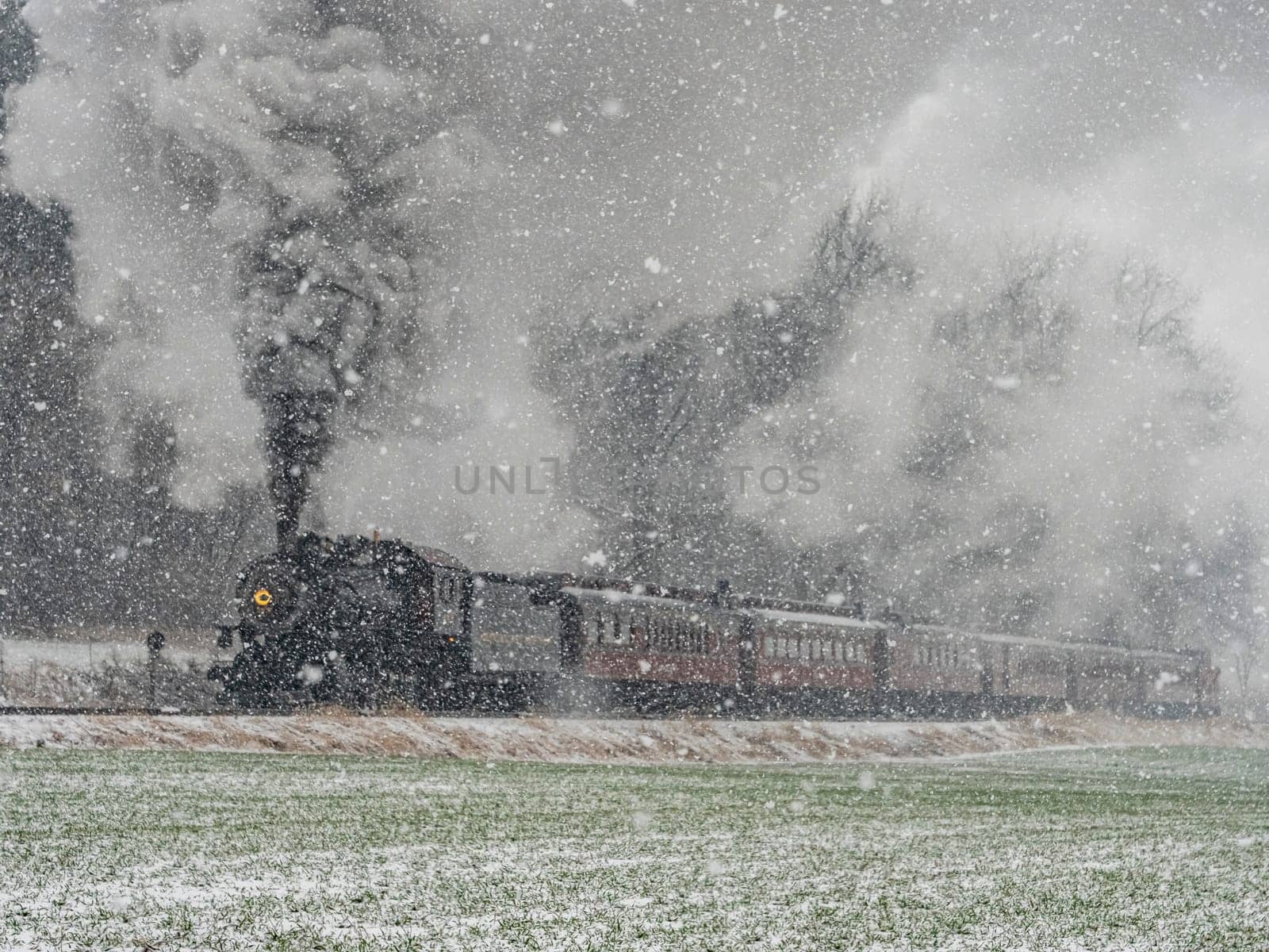 Train is traveling through a snowy field. The steam from the train is visible in the air by actionphoto50