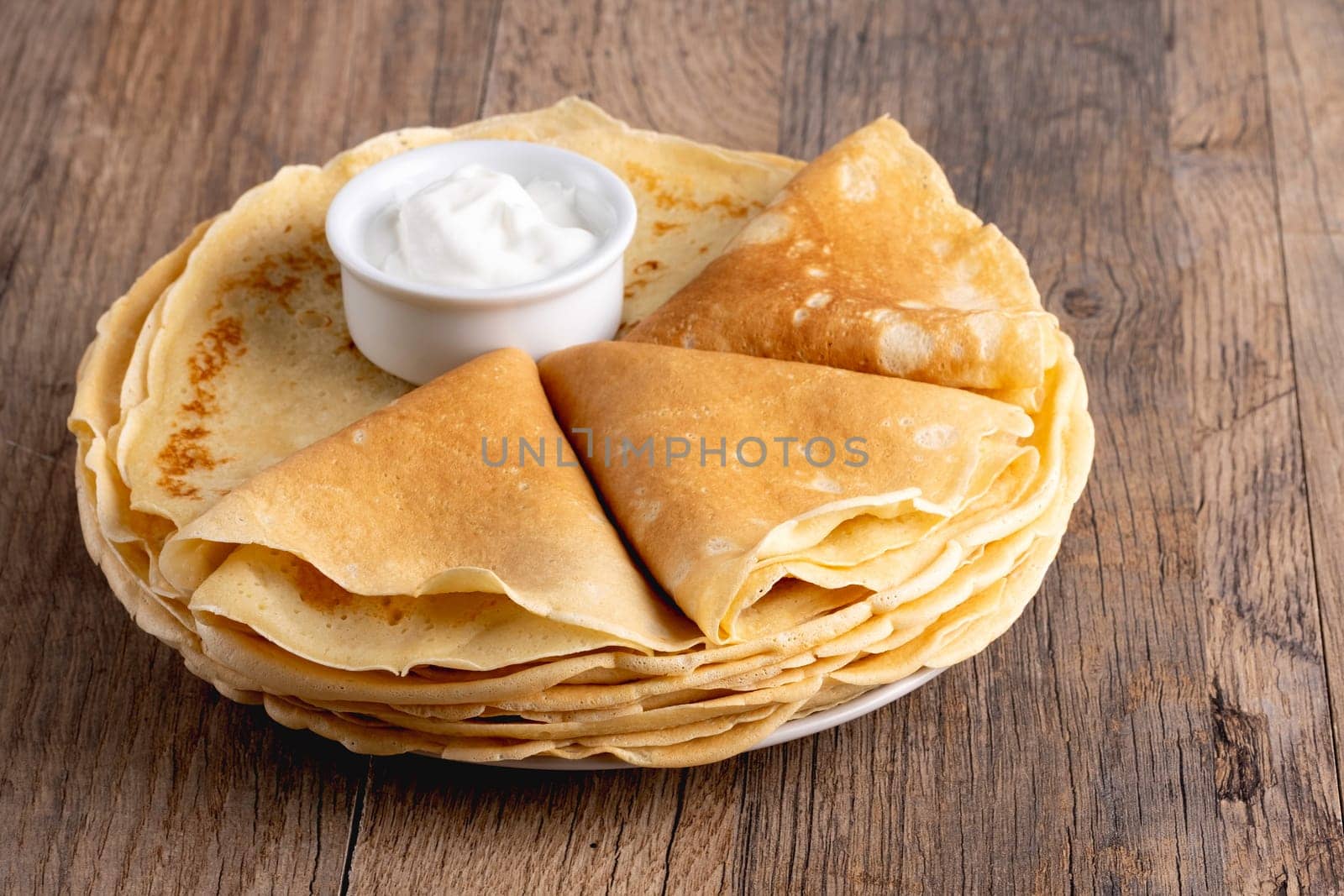 Pancakes with sour cream on a wooden table.