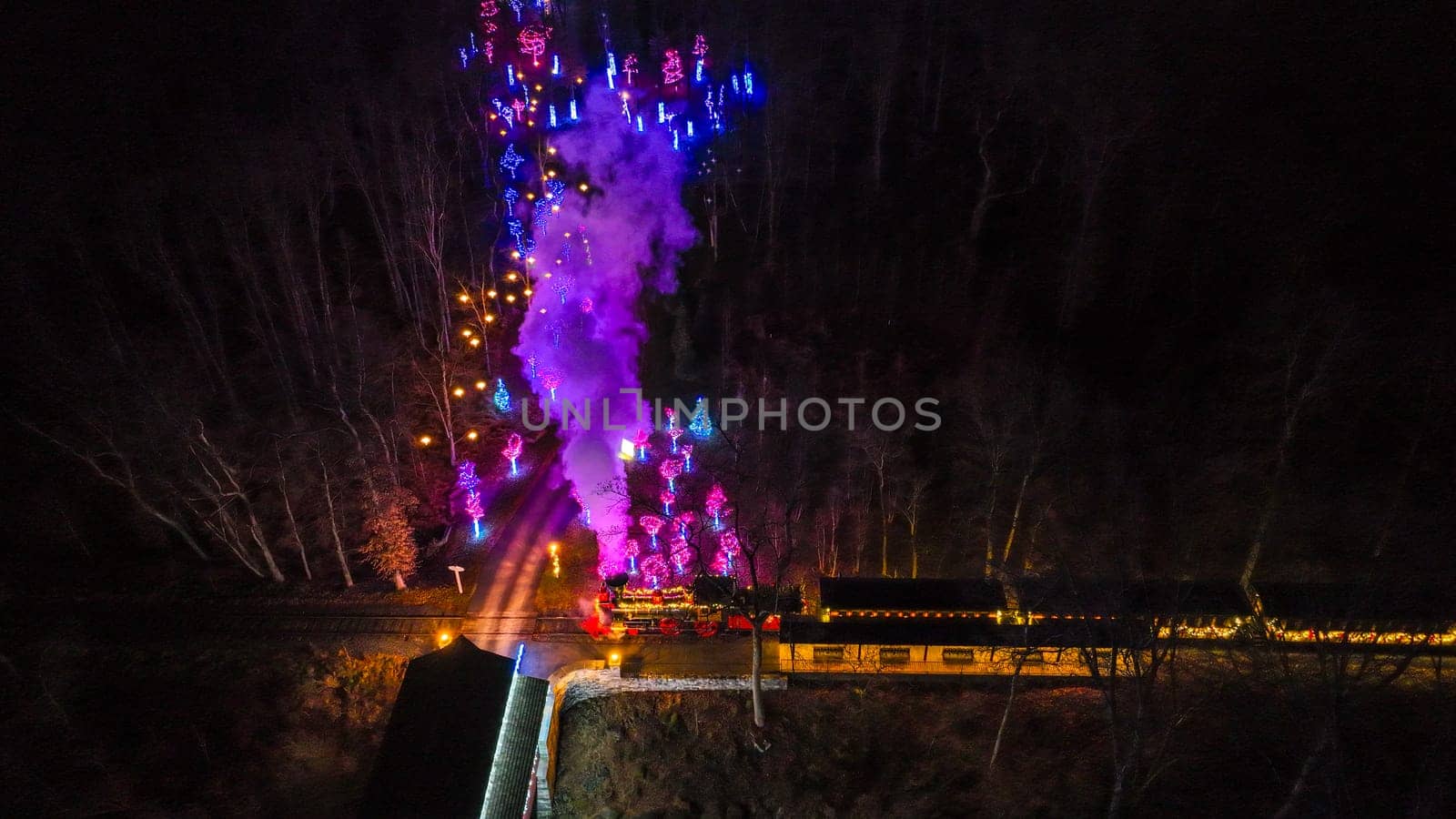 An Aerial View Of A Vibrantly Lit Train Emitting Purple Smoke As It Passes Through A Forested Area At Night.