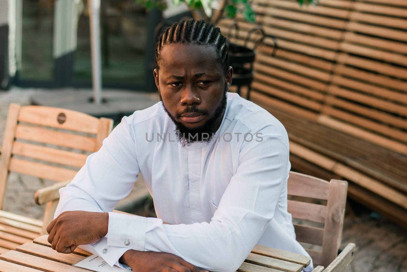 Close up portrait of a happy african american man smiling wearing ethnic dashiki clothes outdoor in summer cafe terrace background. Millennial generation student and youth. by Satura86