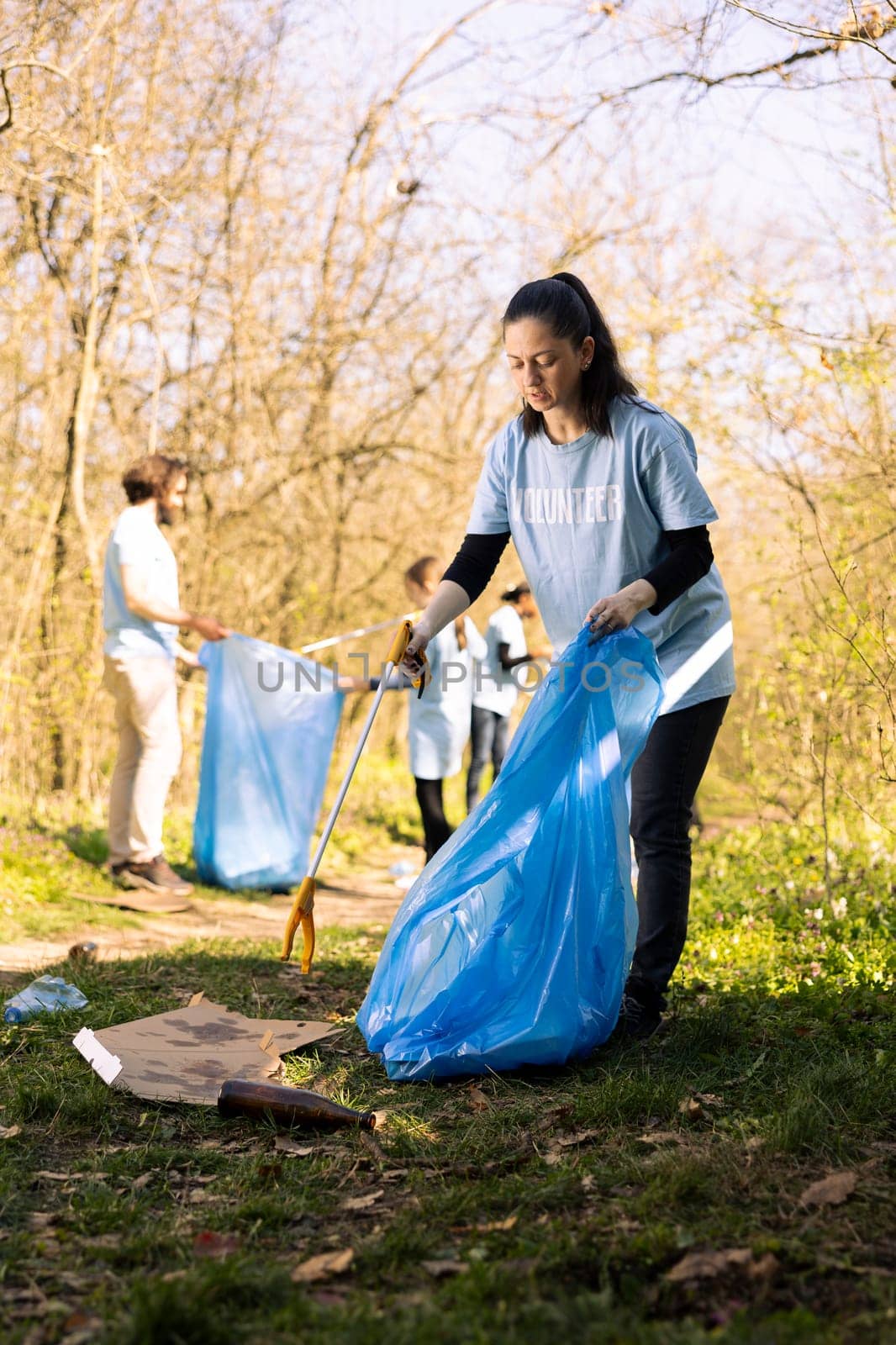 Woman environmentalist collecting junk from the ground to combat pollution within the forest ecosystem, environmental care. Activist doing community service to clean the woods from trash.