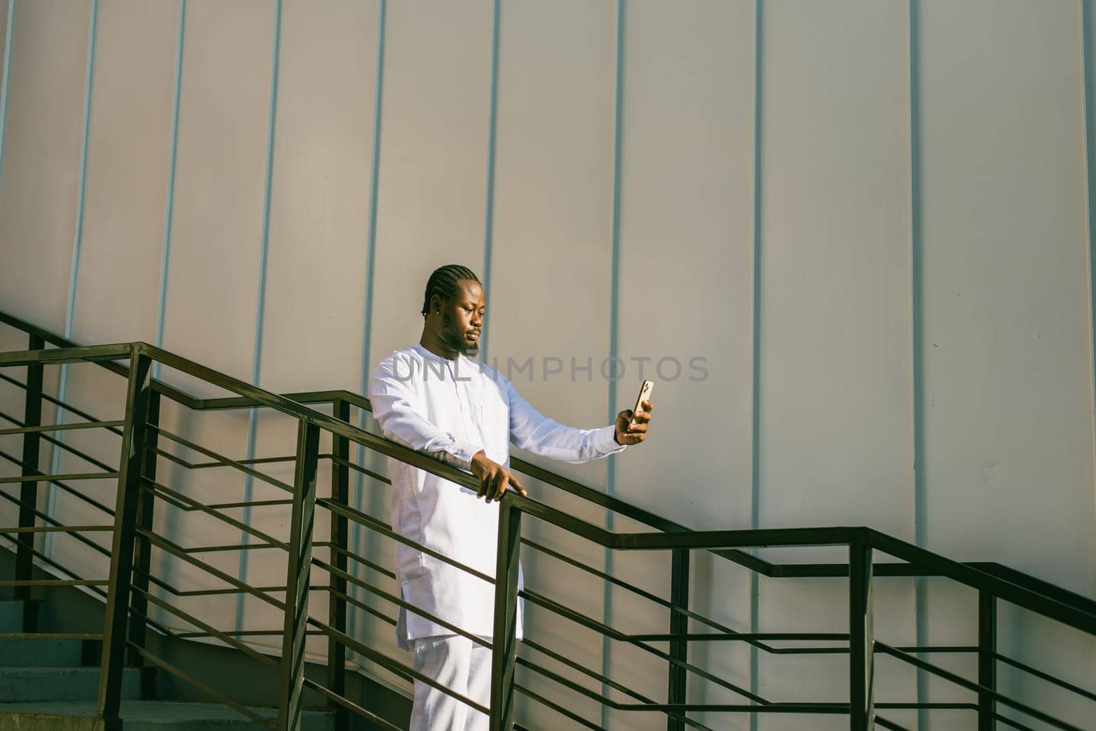 Happy young African American man in dashiki ethnic clothes taking selfie on city street wall background. Millennial generation student and youth. by Satura86