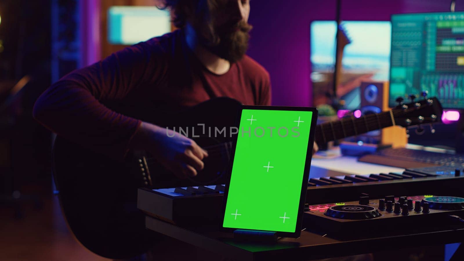 Composer performing acoustical guitar in his home studio, playing and practicing on strings. Musician learning multiple songs on instrument, uses tablet to run greenscreen display. Camera A.