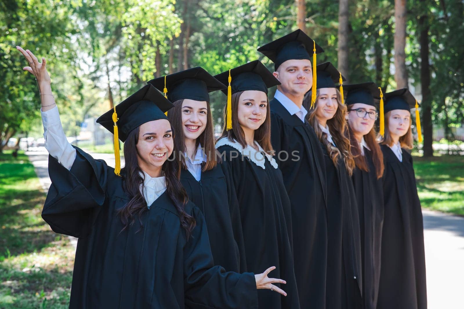 Row of happy young people in graduation gowns outdoors. Students in the park. by mrwed54