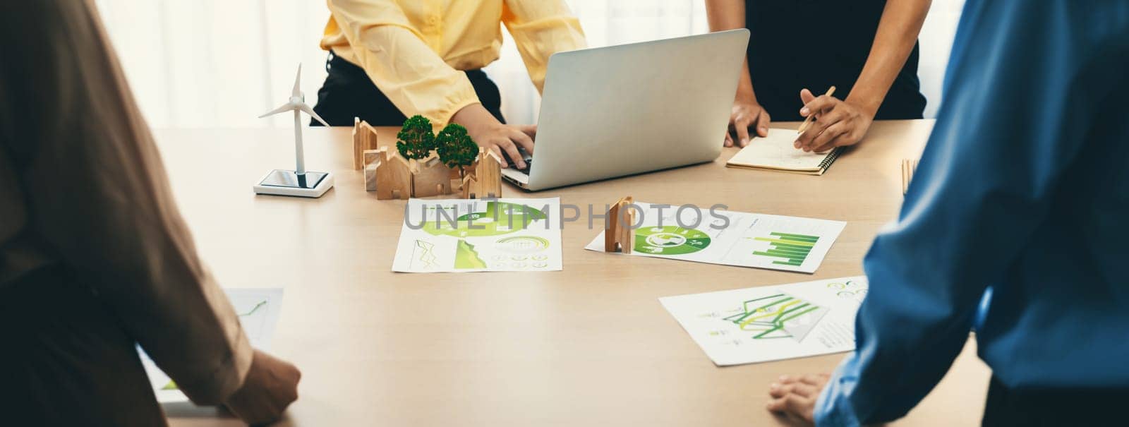 Wooden block represented green city and wind mill represented renewable energy was placed at center of green business meeting table with environmental document. Green business concept. Delineation.