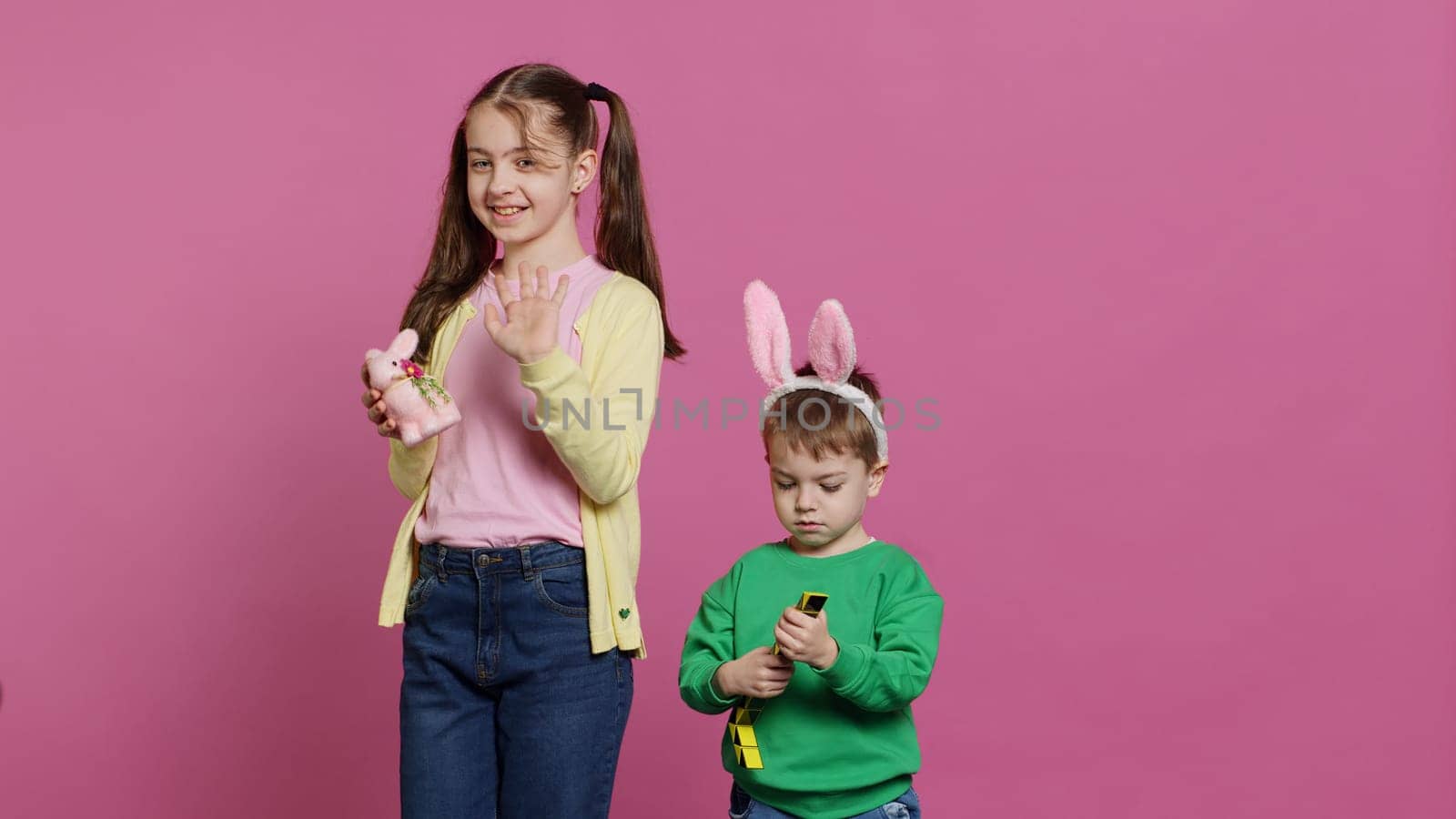 Cute brother and sister posing against pink background in studio by DCStudio