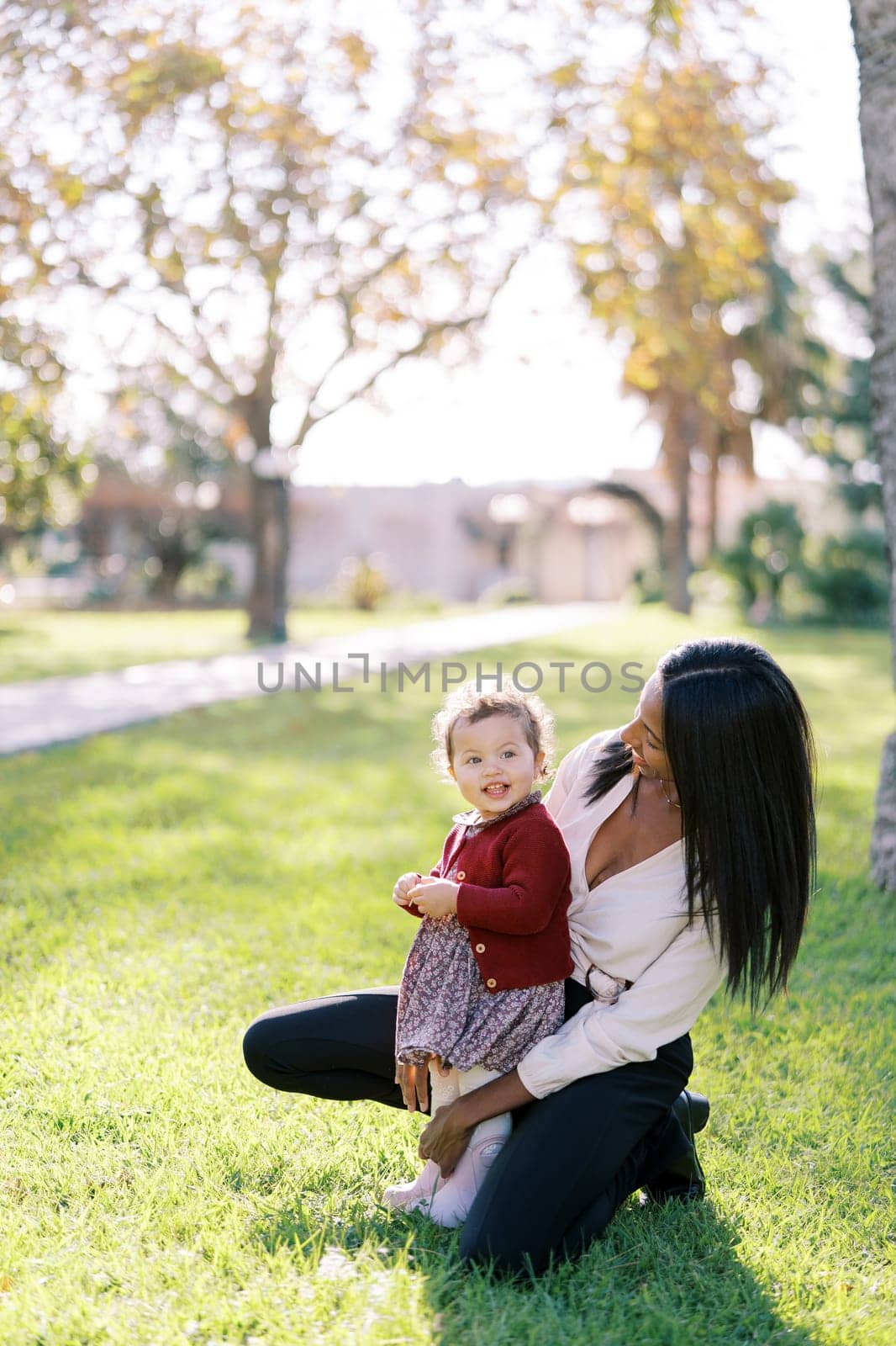 Mom squatted down next to a little smiling girl in a sunny meadow. High quality photo