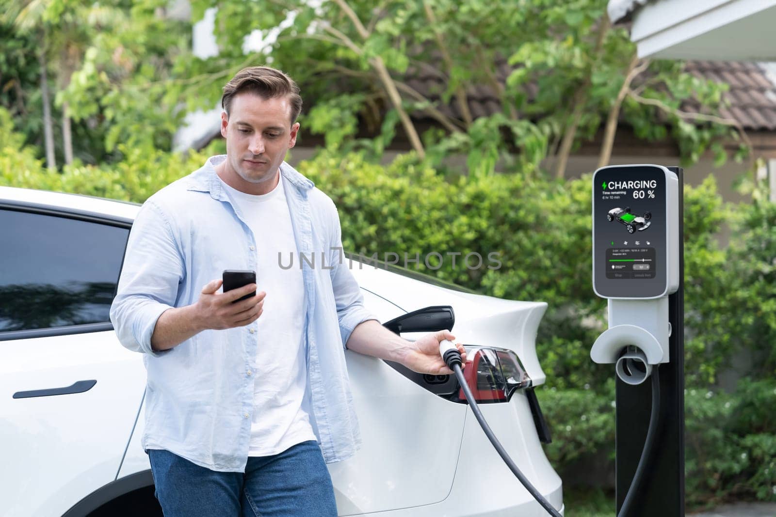 Modern eco-friendly man recharging electric vehicle from home EV charging station. Innovative EV technology utilization for tracking energy usage to optimize battery charging at home. Synchronos