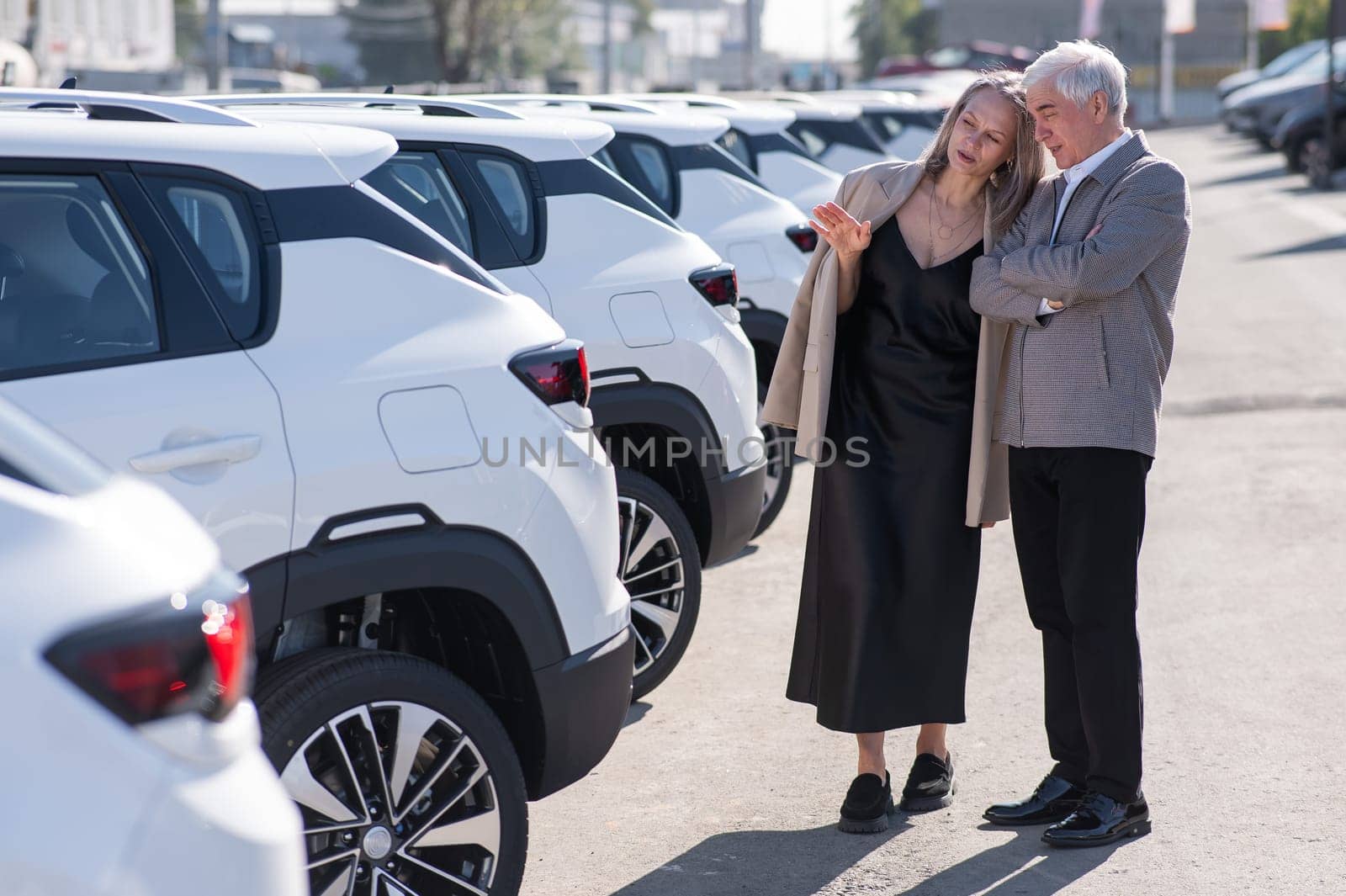 Mature Caucasian couple walks past cars outdoors, choosing a new one. by mrwed54