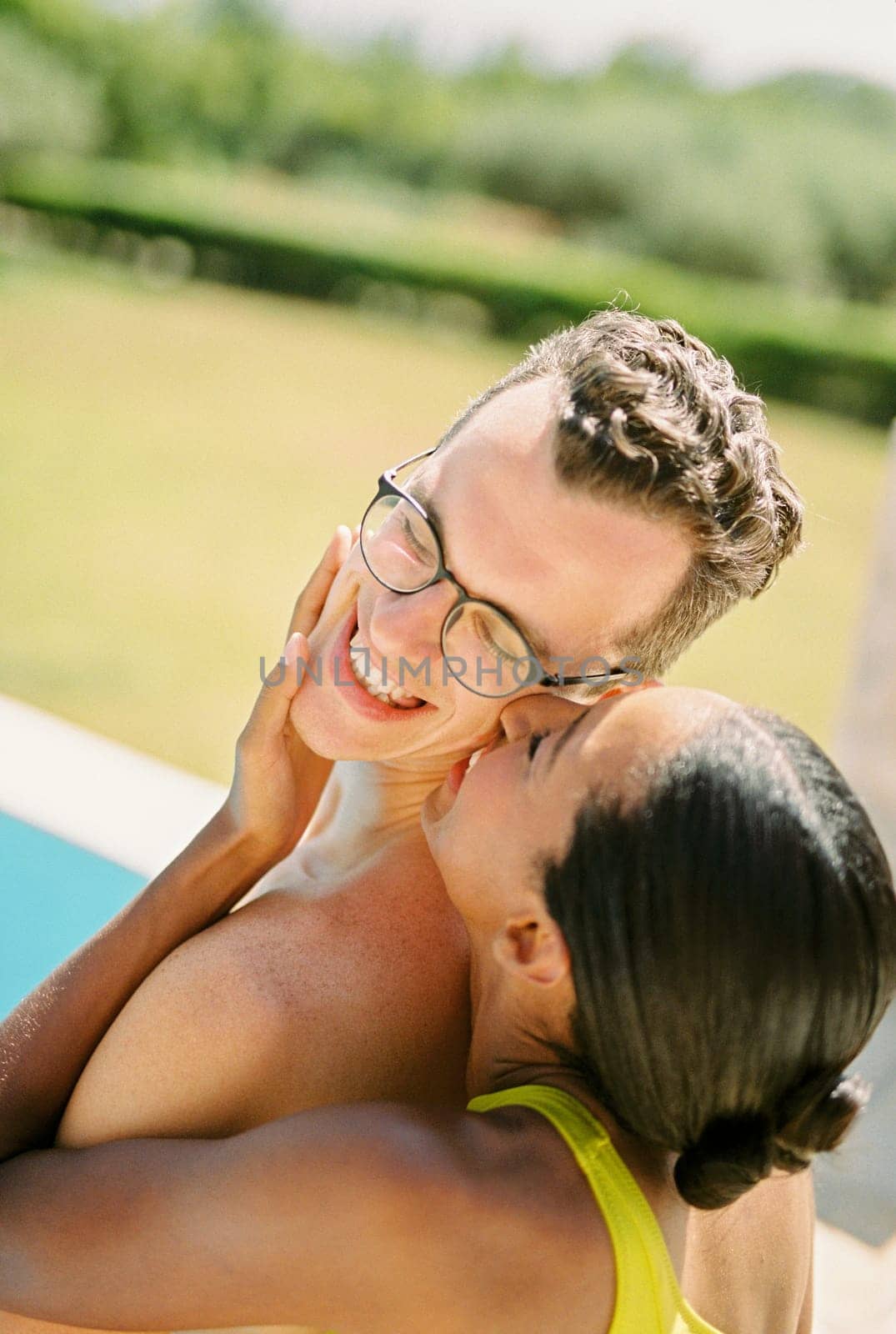 Smiling woman kisses man on the cheek while hugging his face from behind. Back view. High quality photo