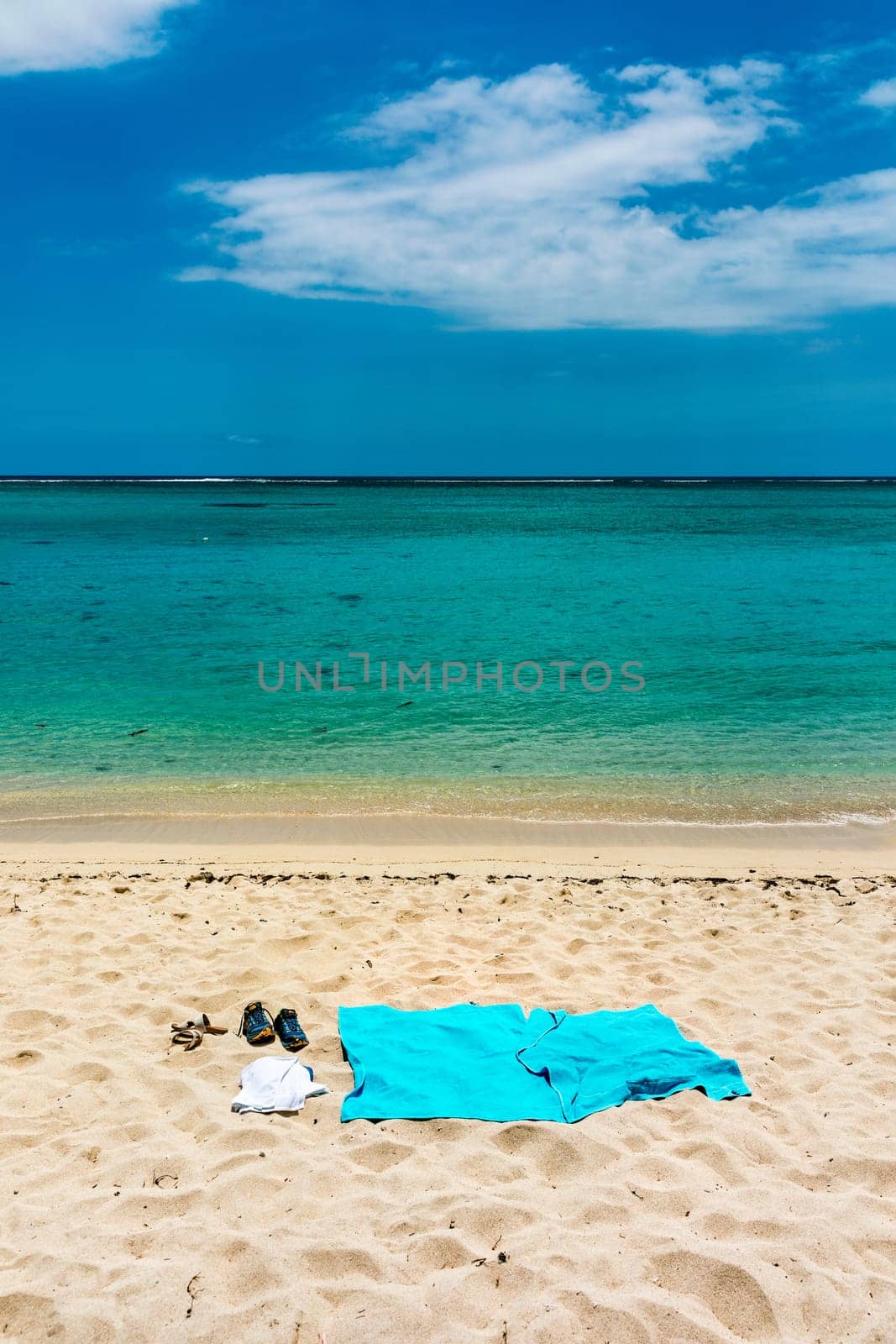 Flip flops and blue beach towel on sand close to the sea